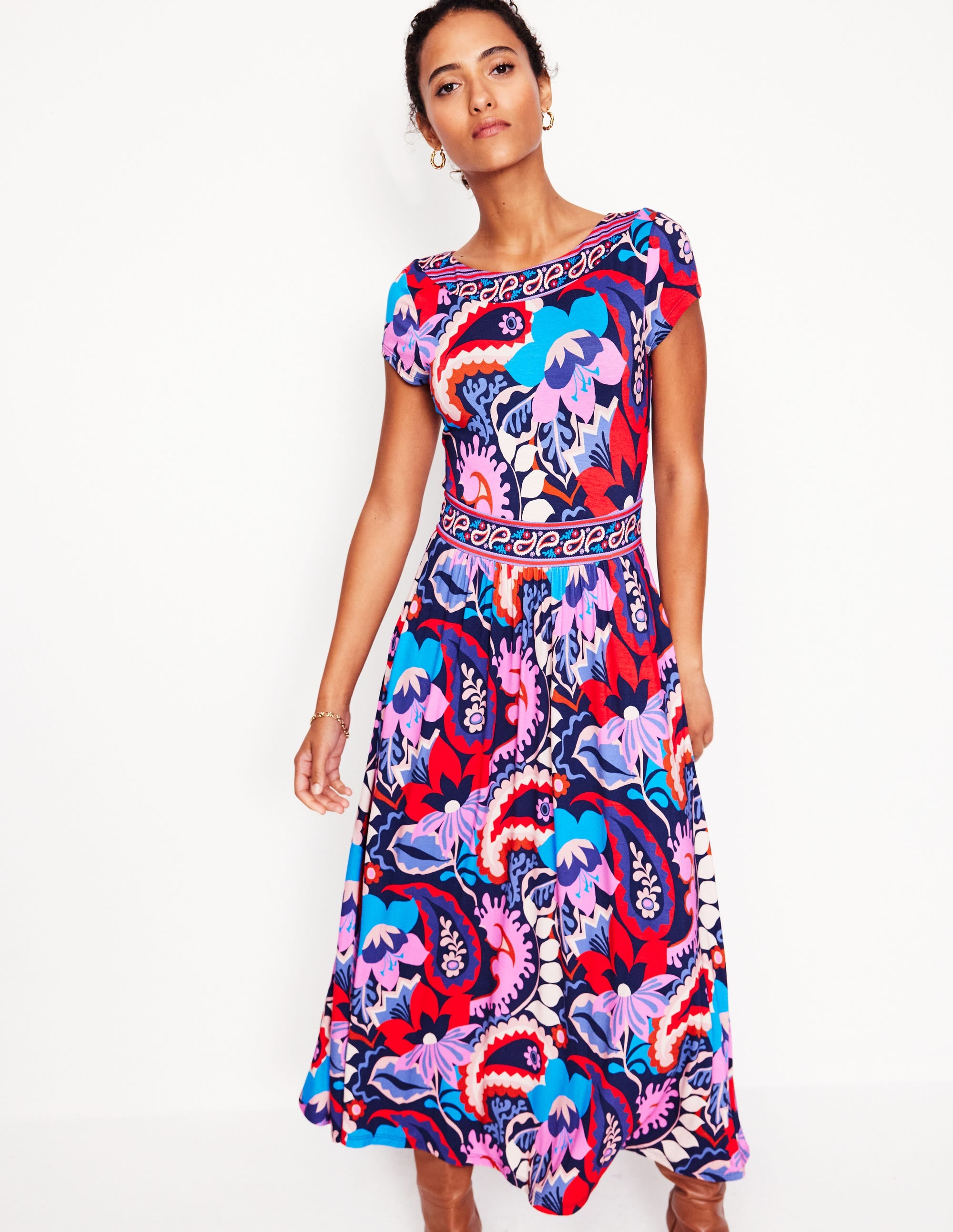 A woman wearing a midi dress with a vibrant botanical paisley pattern in French Navy, featuring a boat neck, cap sleeves, and a wide waistband.