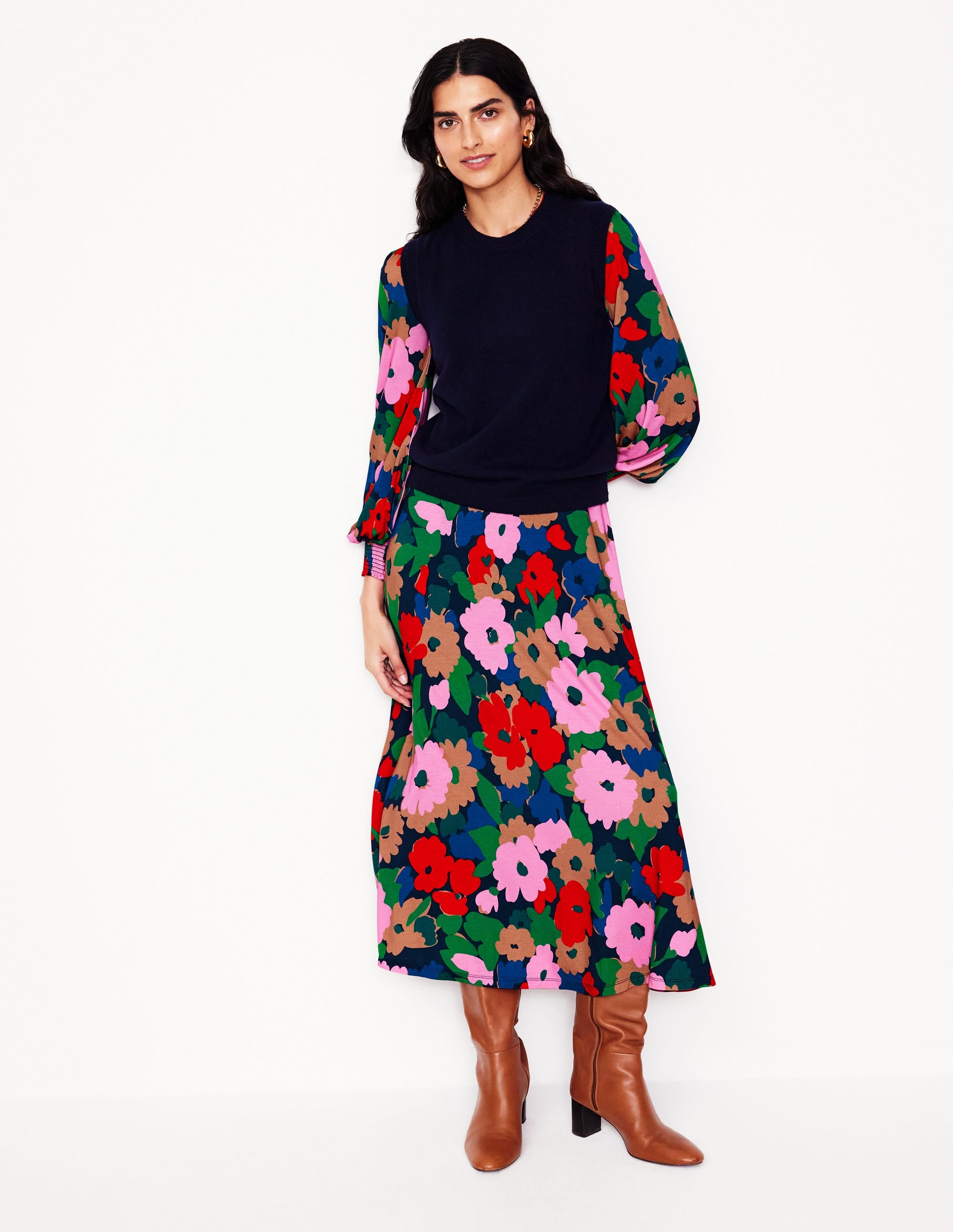 A woman wearing a midi dress with a painterly meadow floral print, smocked waist, notch neckline, and long puffed sleeves, paired with brown boots.