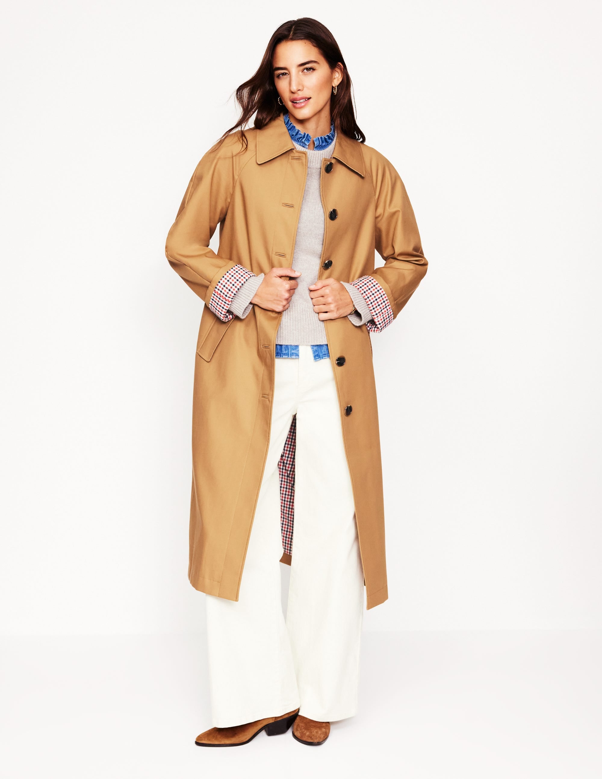 A woman wearing a hazelnut brown oversized water-resistant mac coat with a checked lining visible at the collar and cuffs, button front, and functional pockets.