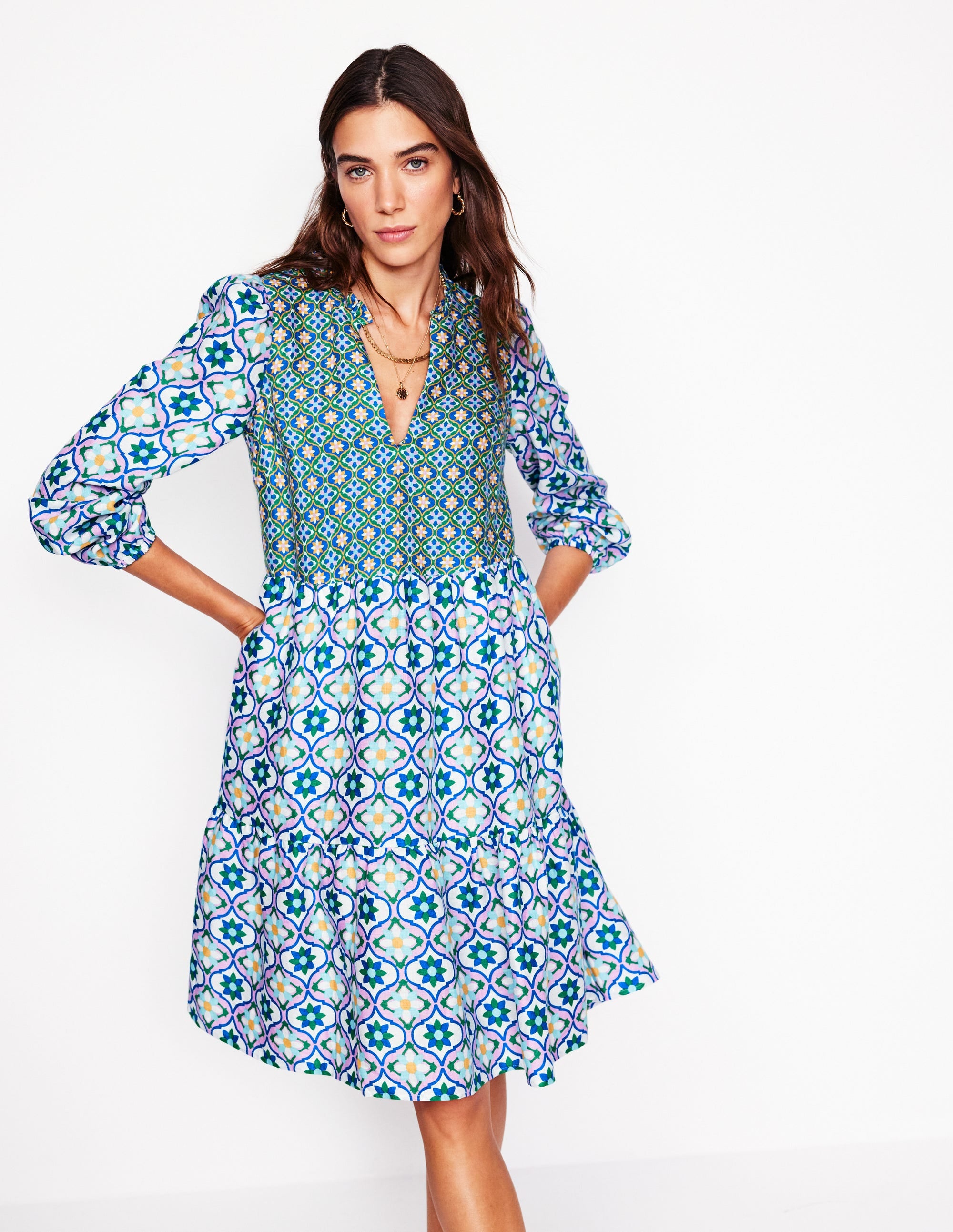 A woman wearing a multicolour floral patterned linen short dress with a tiered design and side pockets.
