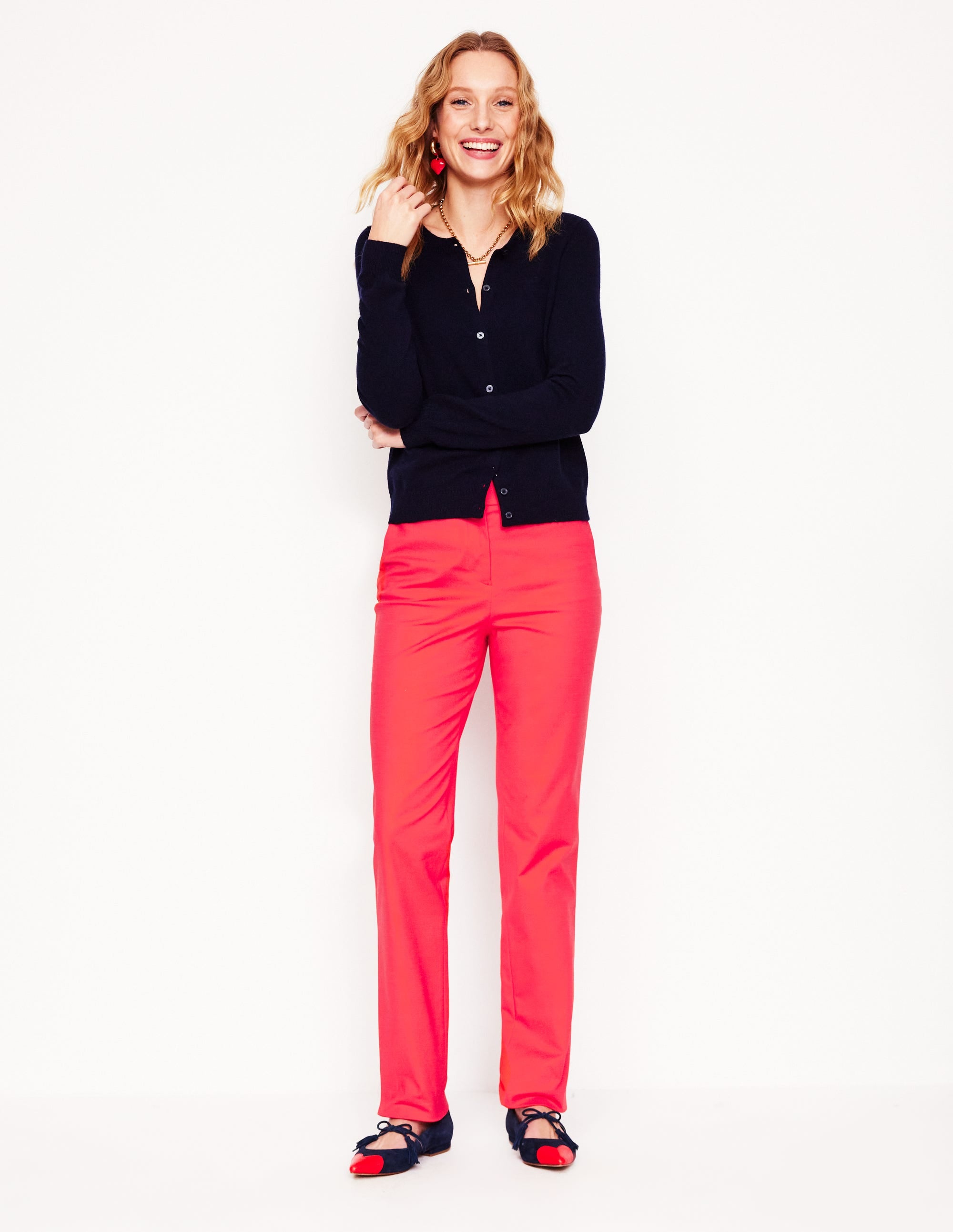 A pair of women's trousers in Strawberry Tart Red with a tapered fit, sitting at the natural waist, made from stretch fabric, with functional pockets, shown on a woman with a relaxed fit over hips and thighs.