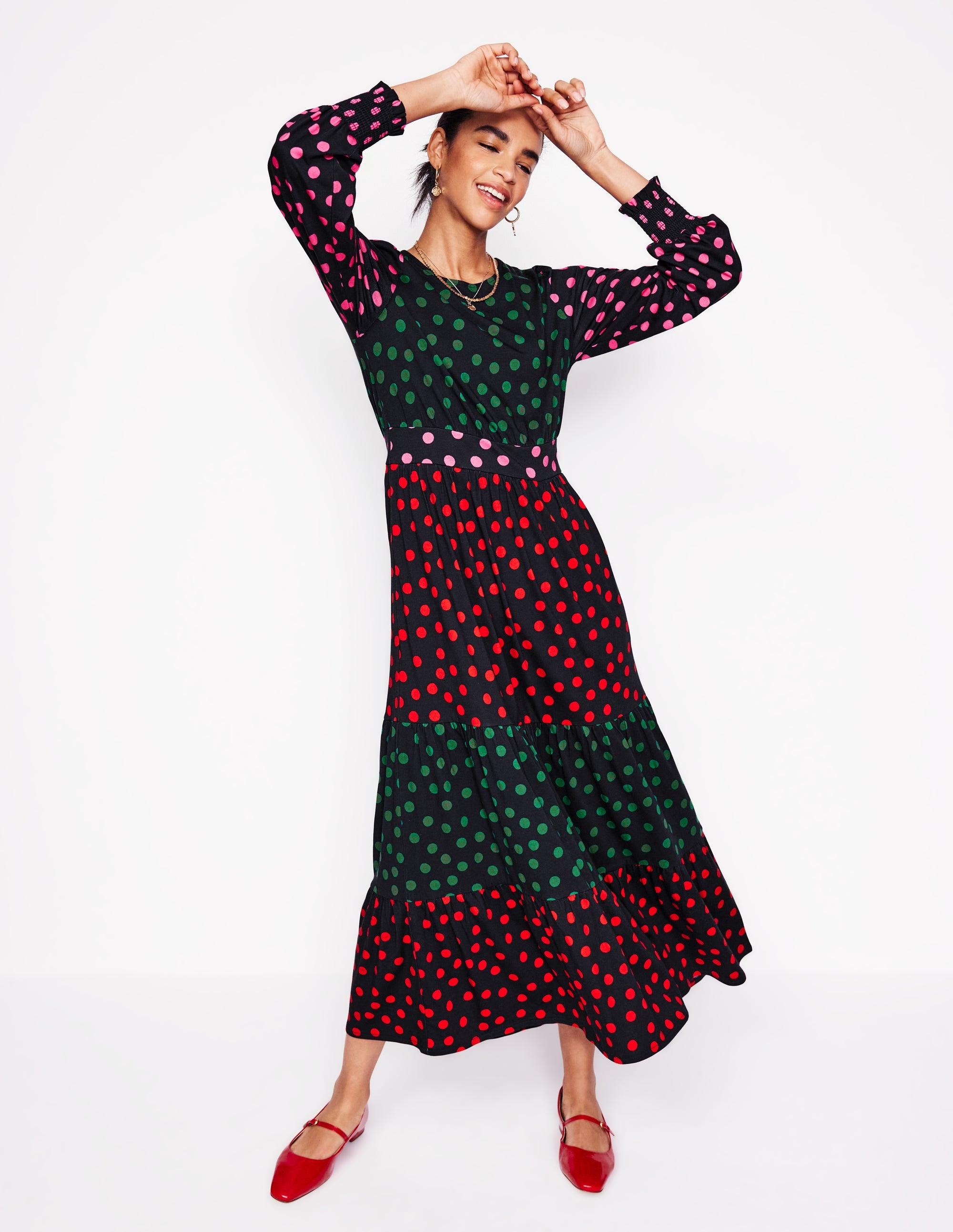 A woman wearing a long, tiered maxi dress with a multicolour abstract dot pattern, blouson sleeves with frills, and side pockets.