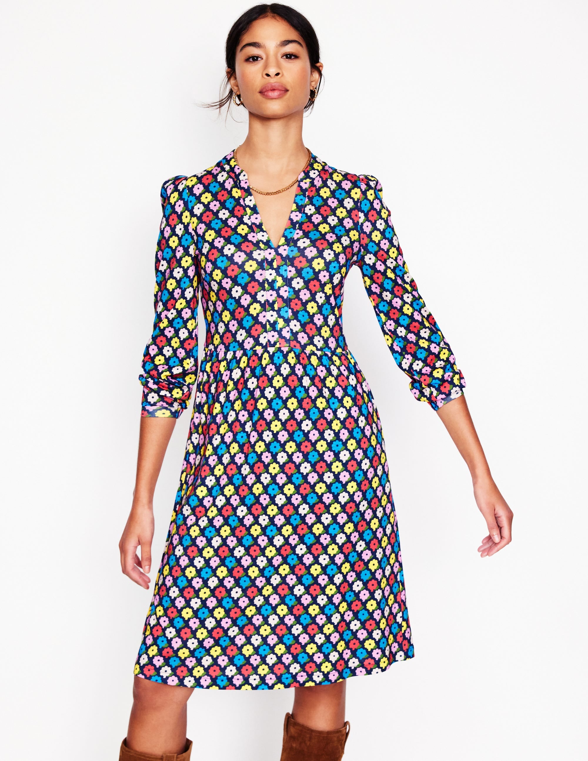 A woman wearing a knee-length jersey dress with a colorful pop daisy print, long sleeves, and a V-neckline.