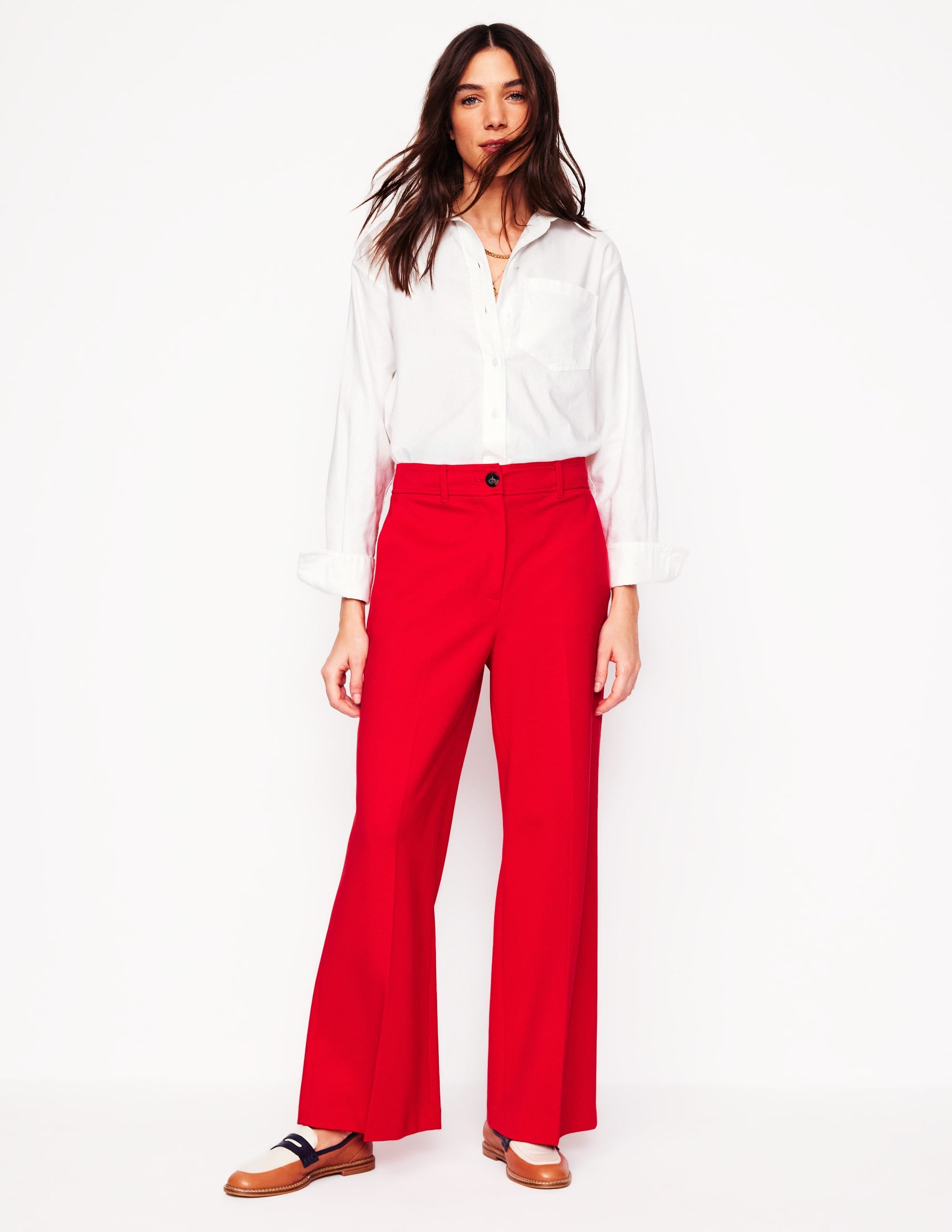 A woman wearing bright red cropped trousers with a white shirt tucked in, standing against a plain background.