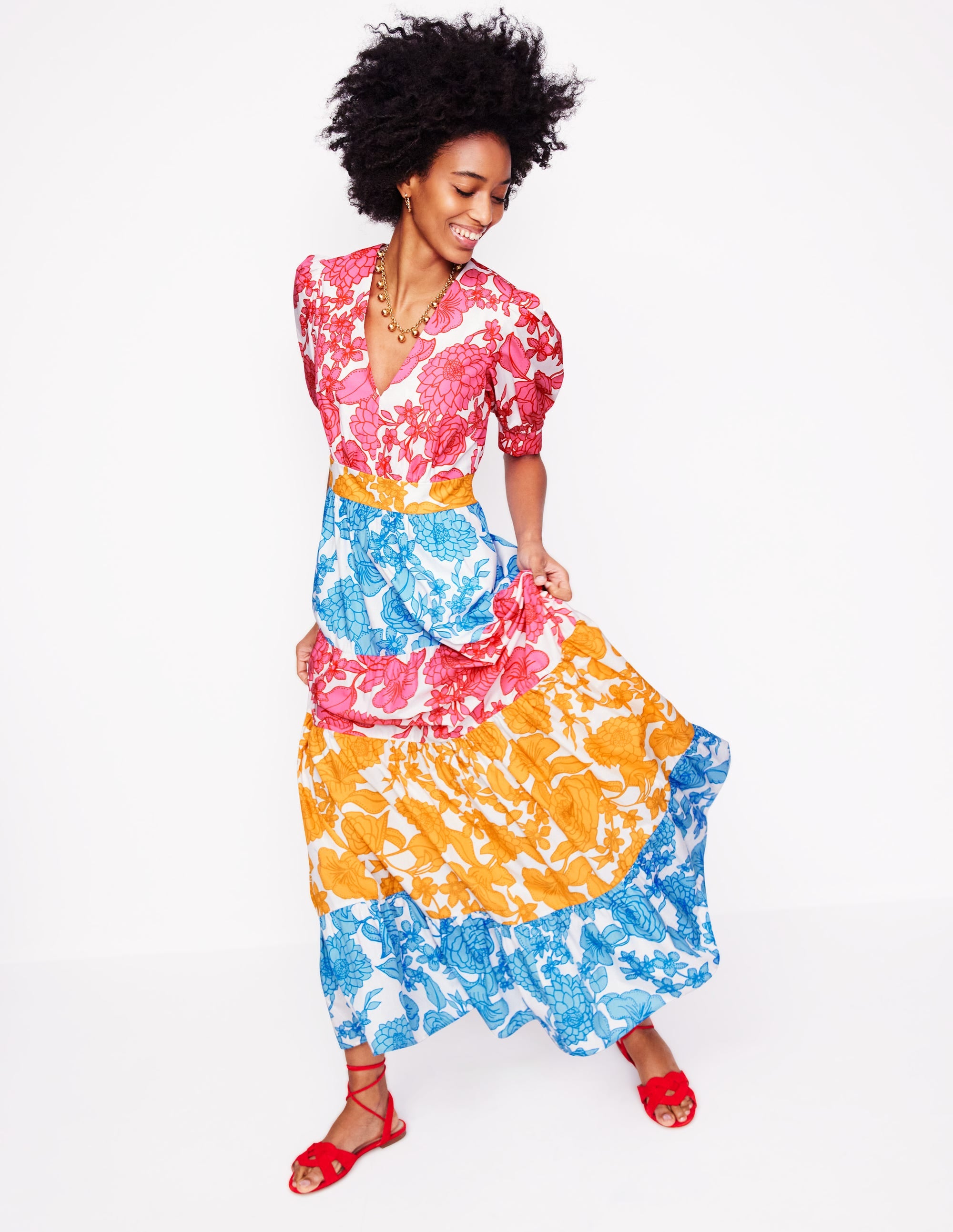 A woman wearing a multicolour floral maxi dress with puff sleeves, tiered skirt, and V-neckline, standing against a white background.