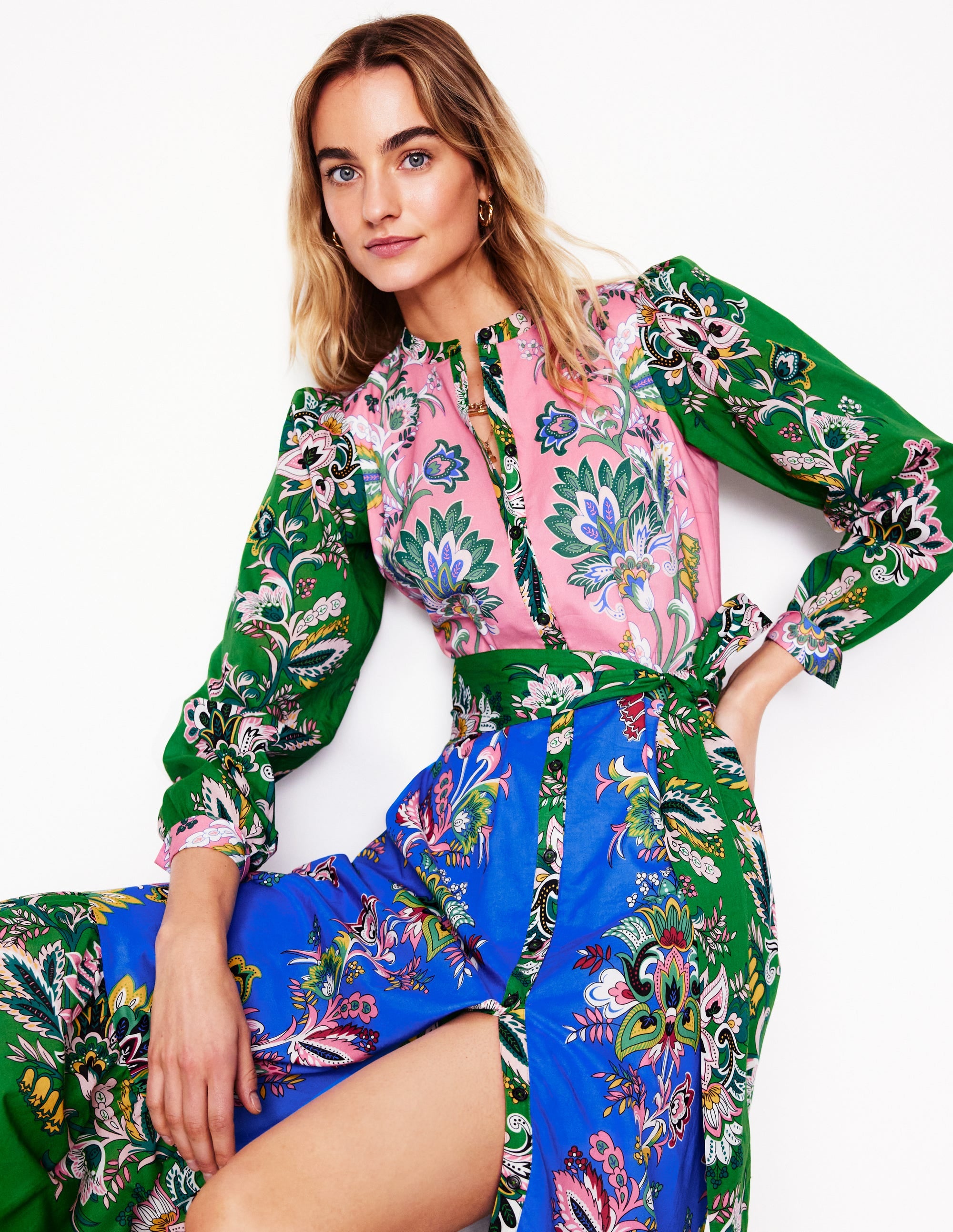 A woman wearing a multicolour floral shirt dress with blouson sleeves, tiered skirt, tie belt, and pockets.