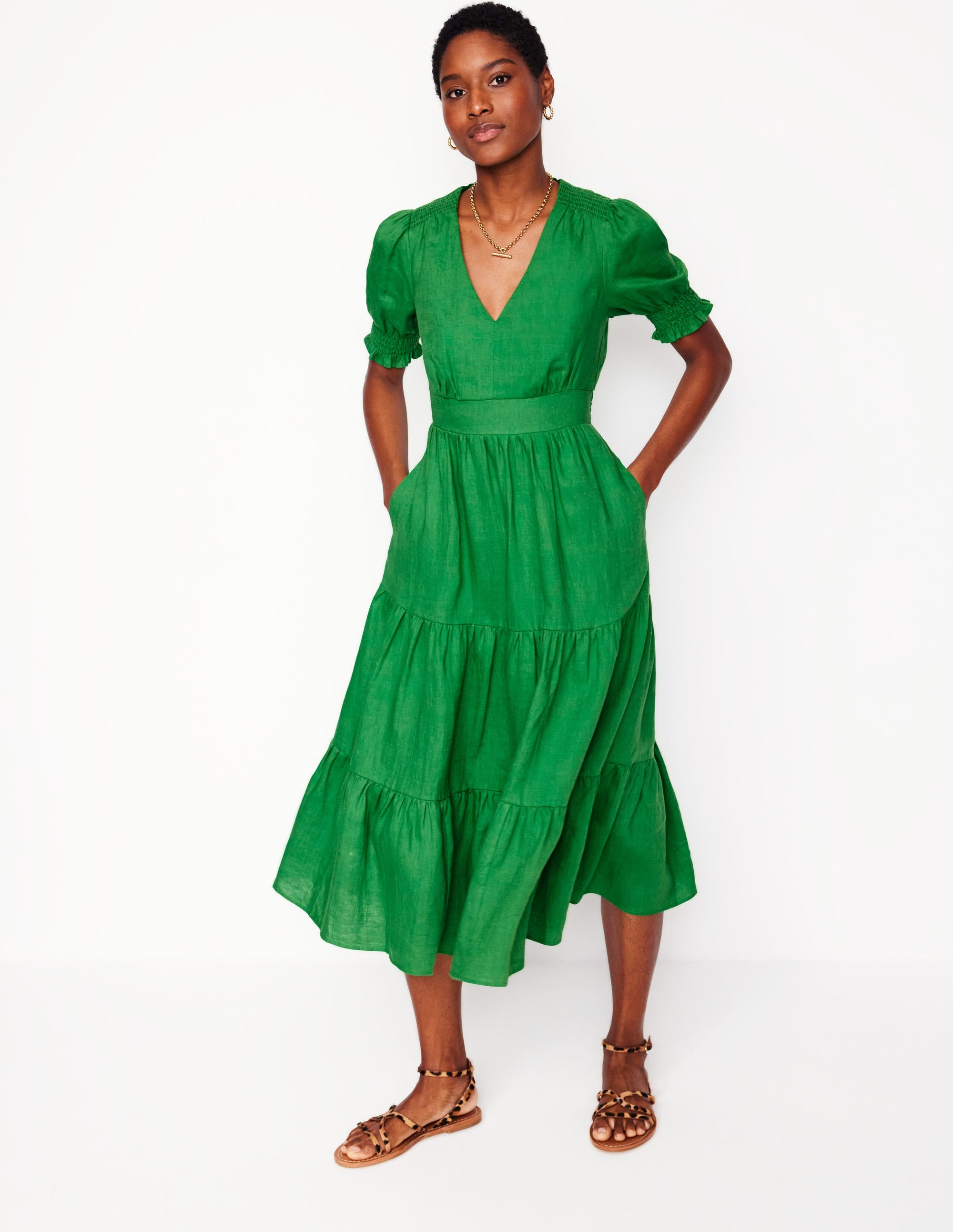 A woman wearing a bright green linen midi dress with puff sleeves and a tiered skirt, standing against a plain background.