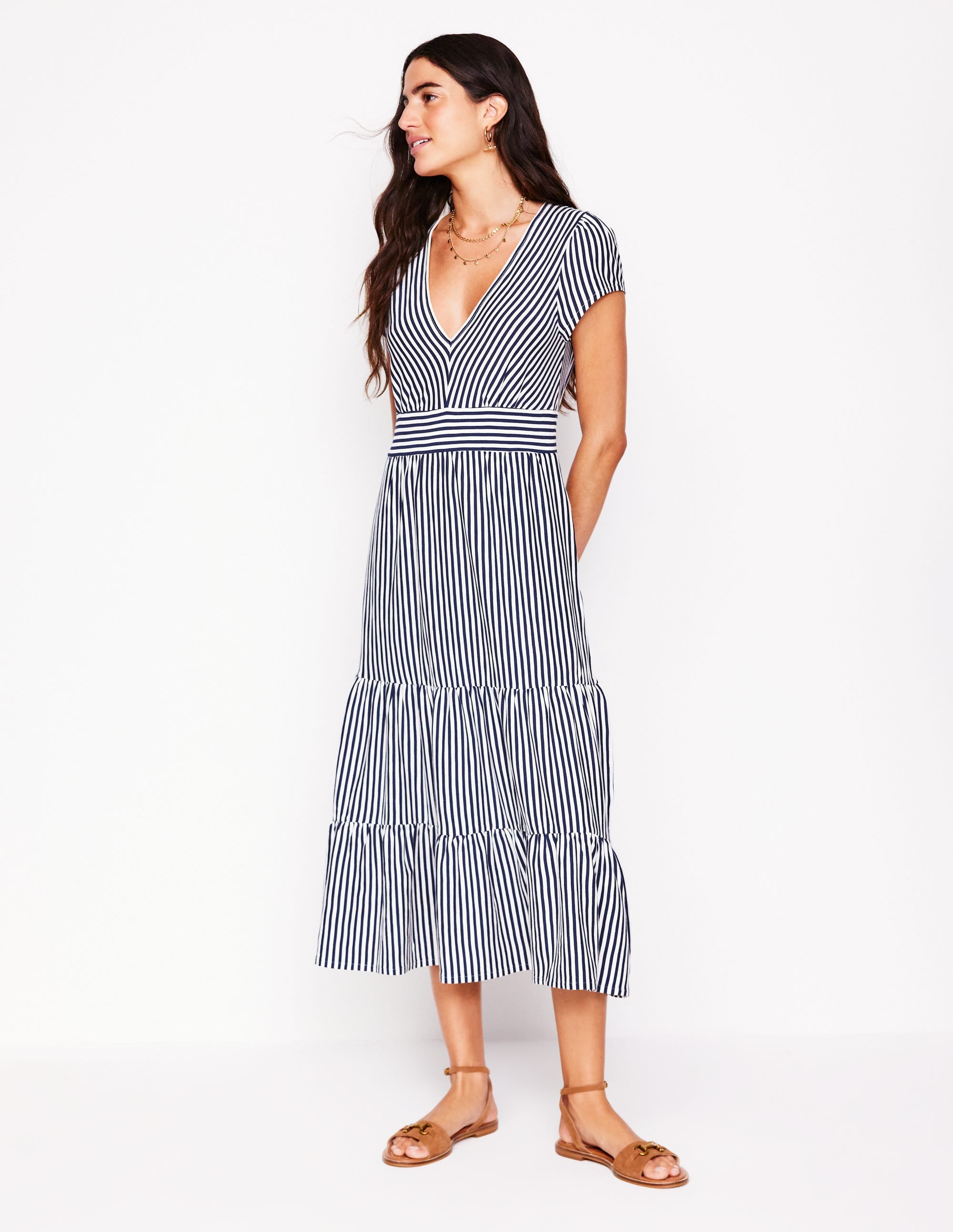 A woman wearing a navy and ivory striped tiered jersey dress with a V-neckline, cap sleeves, and side pockets, standing against a white background.