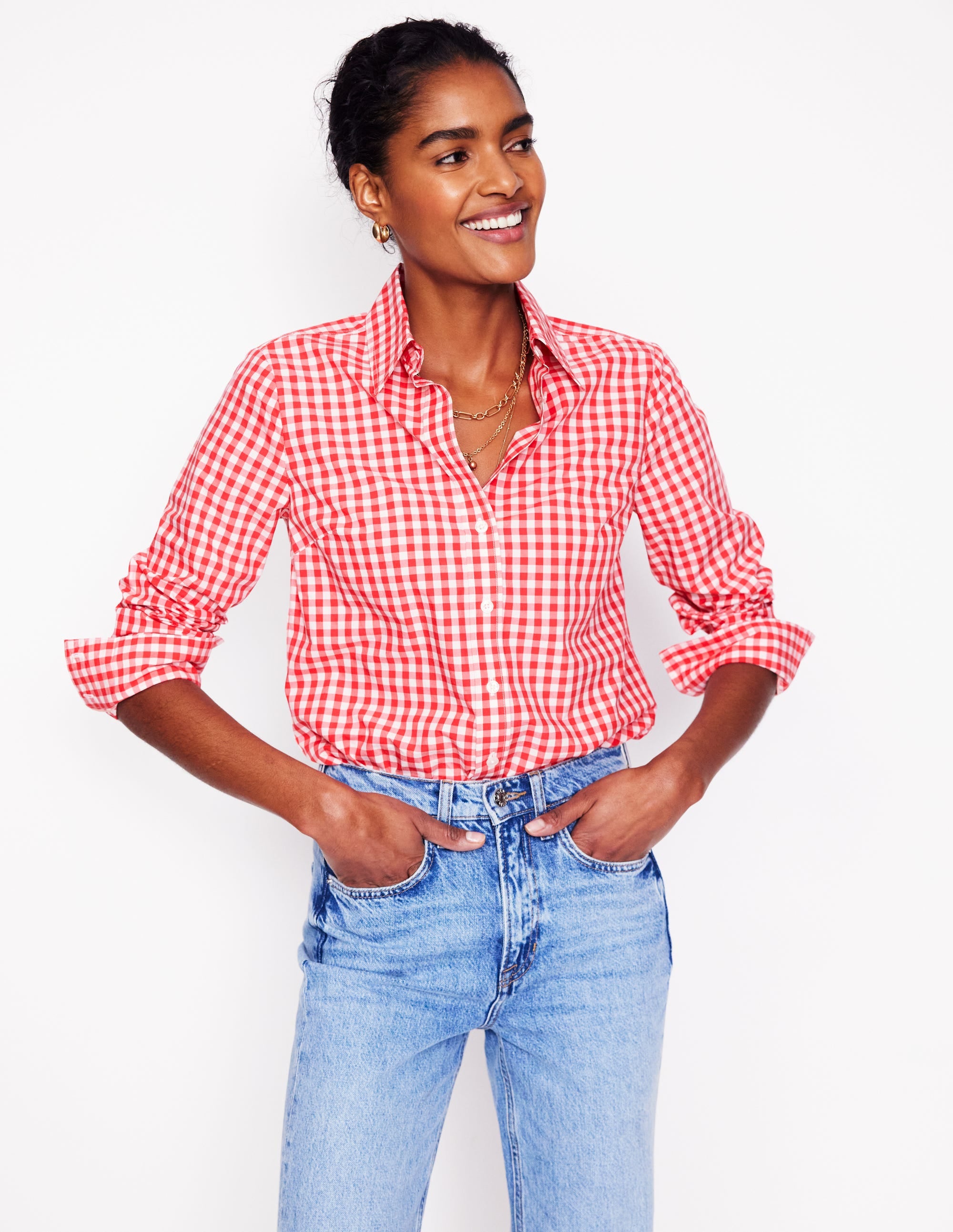 A woman wearing a red and white gingham cotton shirt with long sleeves and a curved hem, styled casually.