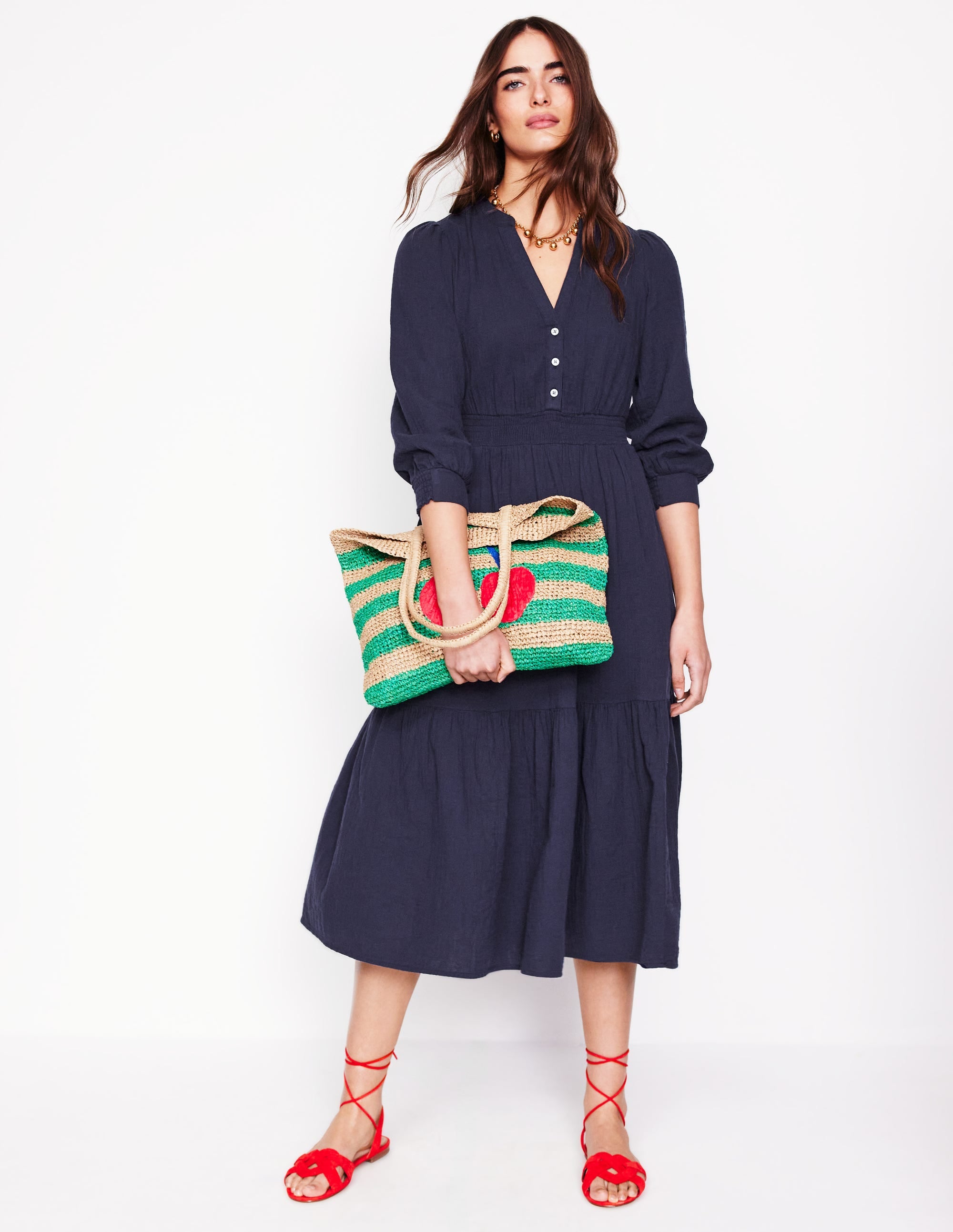 A woman wearing a navy blue midi dress with long puffed sleeves, a button-down front, and side pockets, standing against a white background.