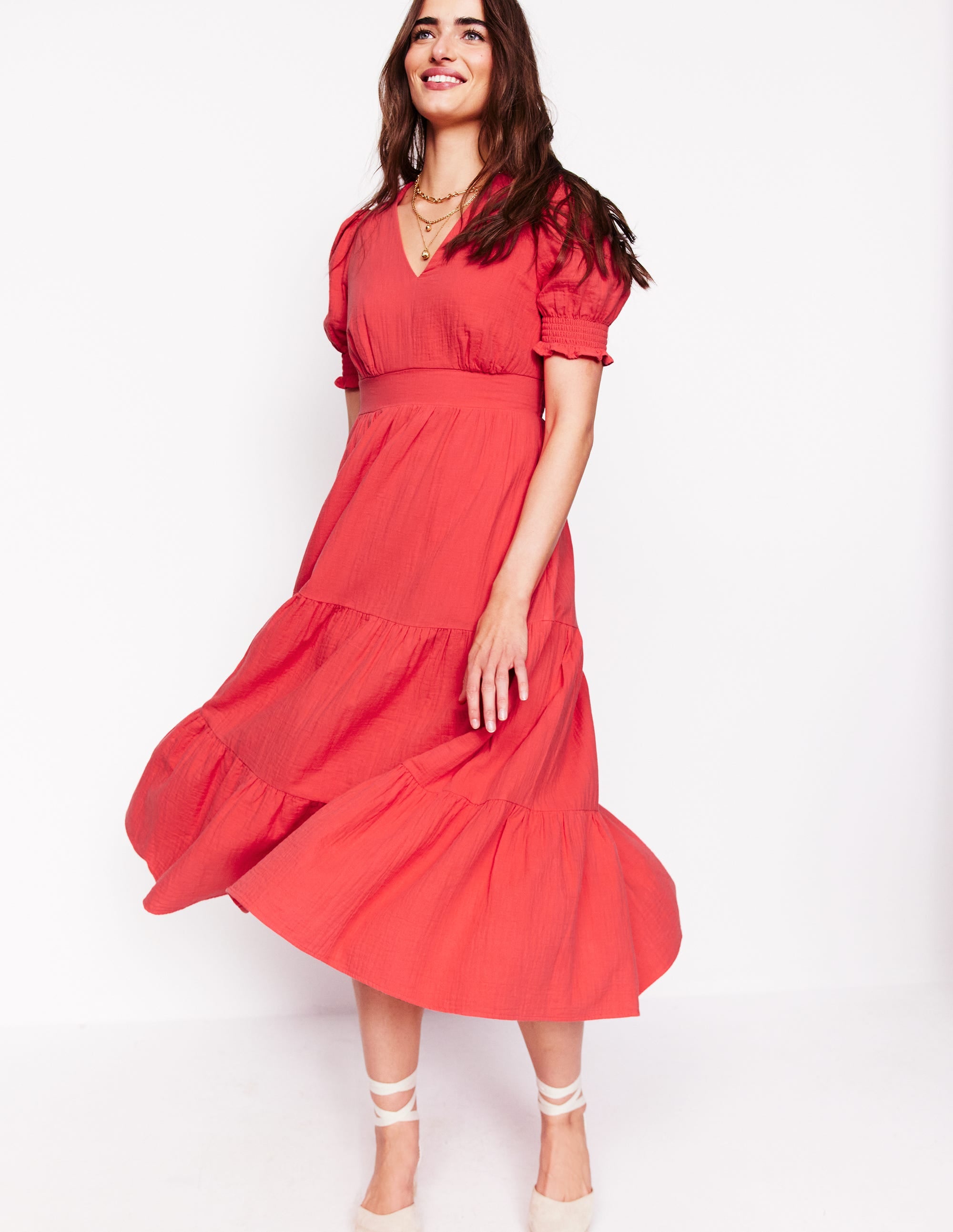 A woman wearing a red midi dress with a V-neck, short puffed sleeves with elastic cuffs, a fitted waistband, and a tiered skirt that reaches mid-calf.