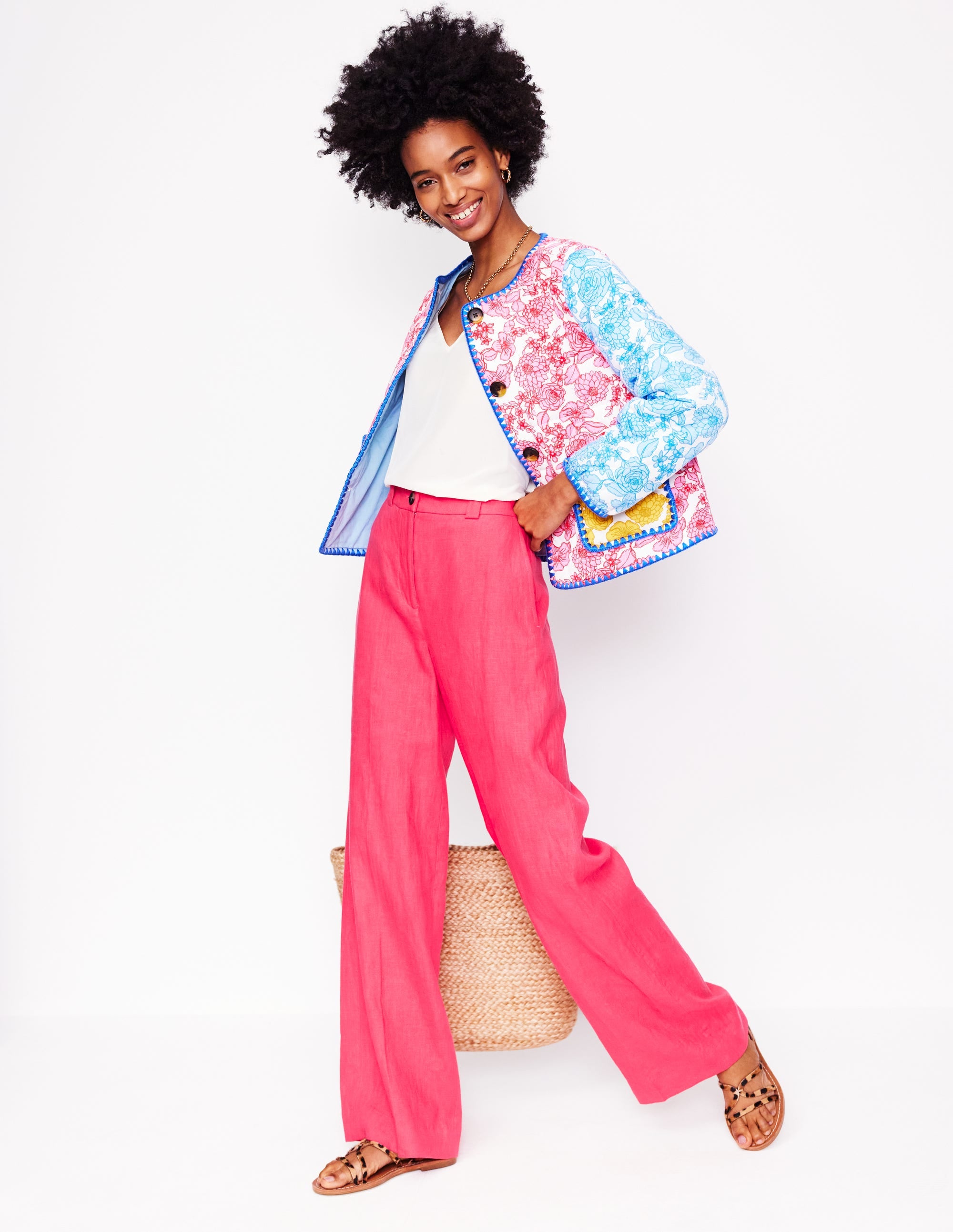 A woman wearing pink wide-leg linen trousers with a high waist, paired with a white top and a colorful floral jacket.