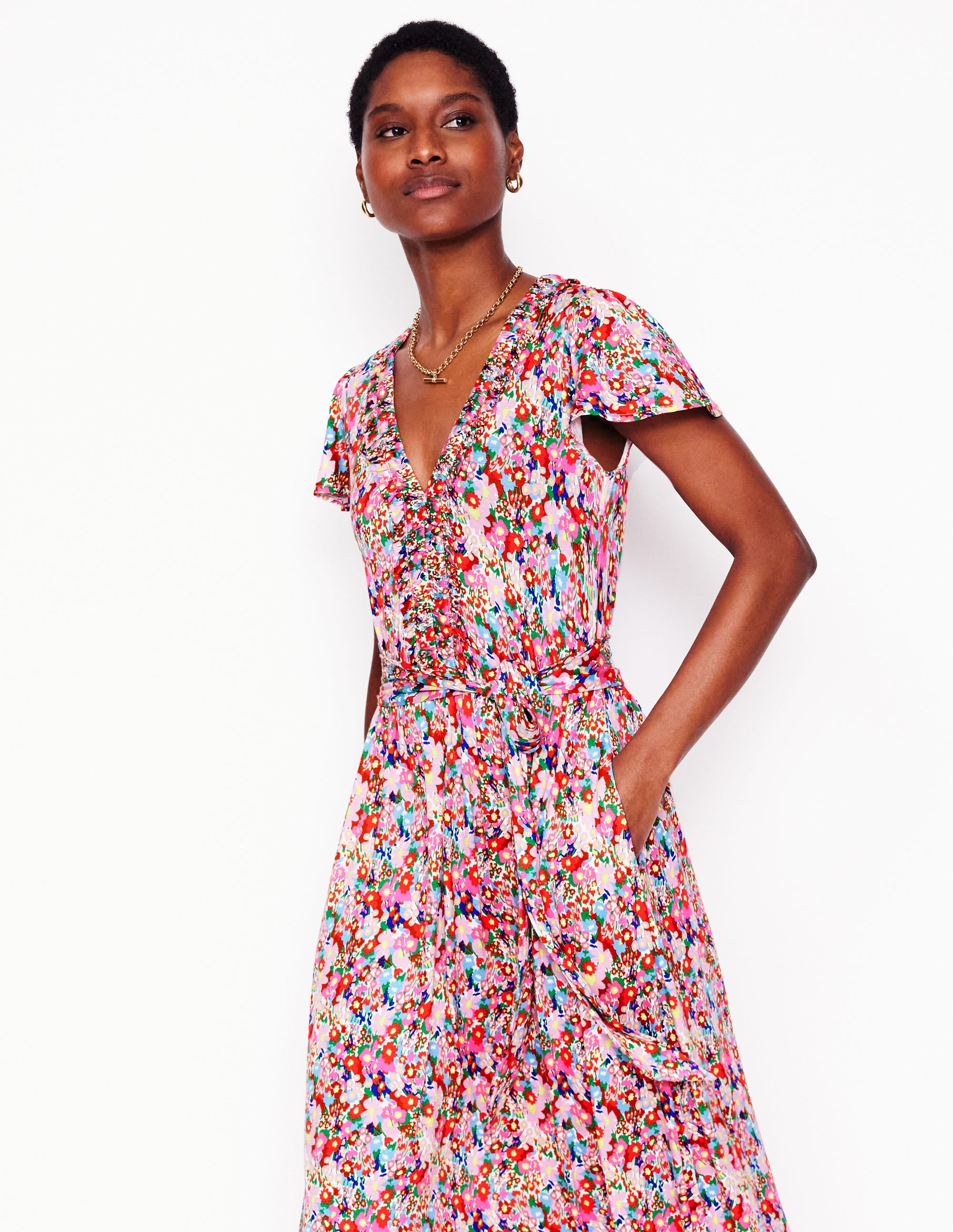 A woman wearing a colorful floral midi dress with short flutter sleeves, side pockets, and a flowy skirt.