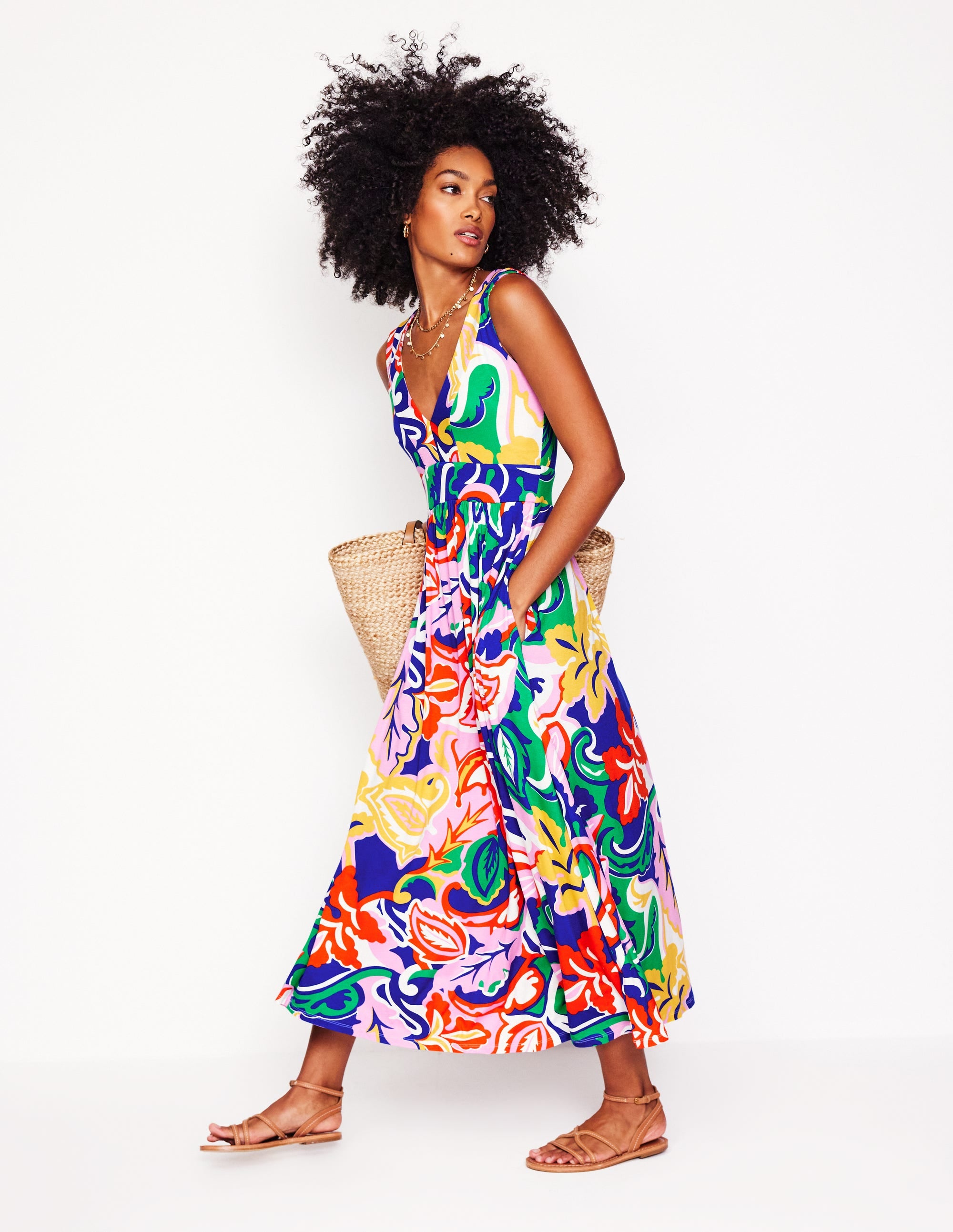 A woman wearing a colorful, patterned maxi dress with a tiered design, V-neckline, and side pockets, standing against a plain background.