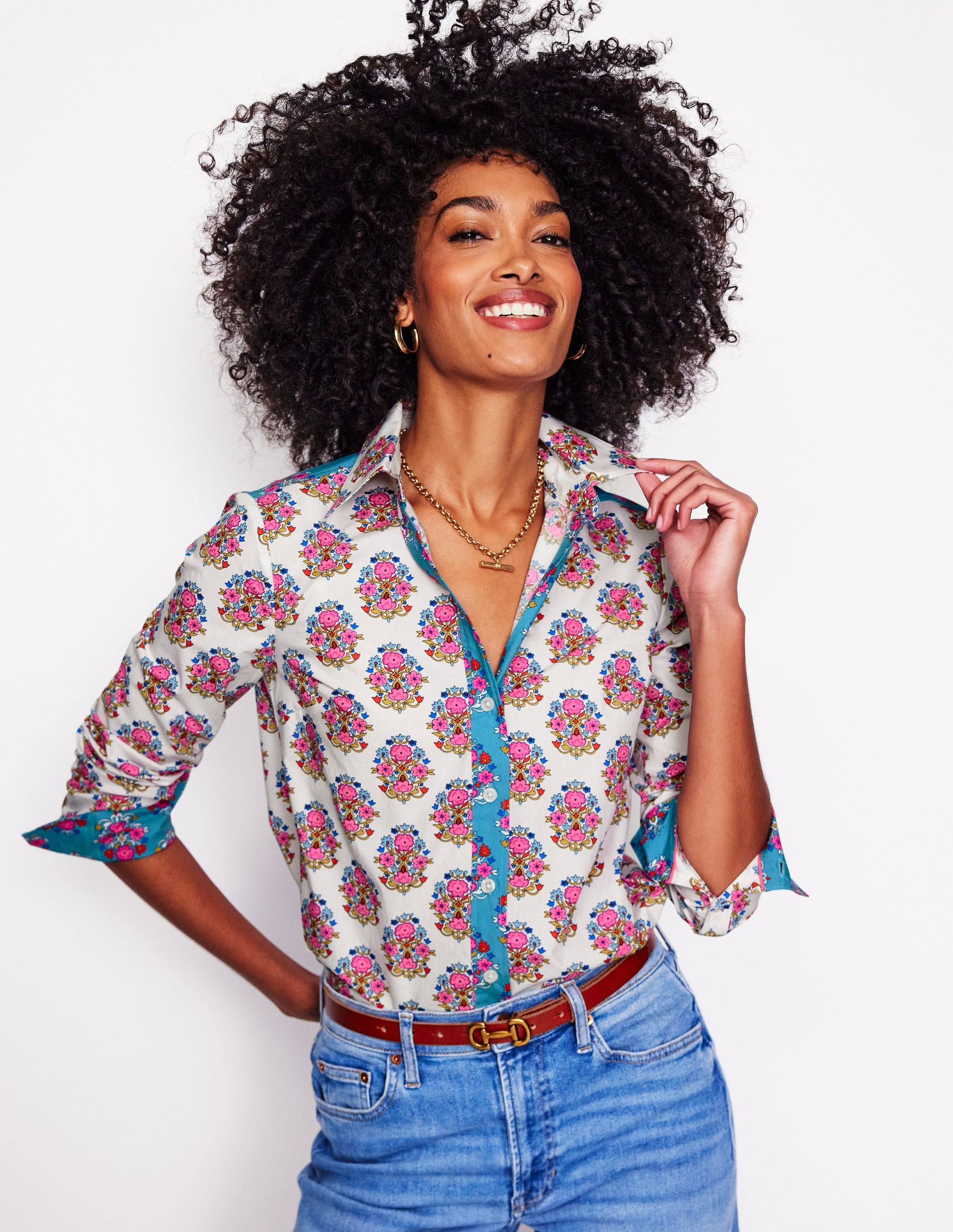 A woman wearing a women's cotton shirt in ivory with a floral pattern, featuring pink, purple, and green flowers, with a classic button-down style and curved hem.