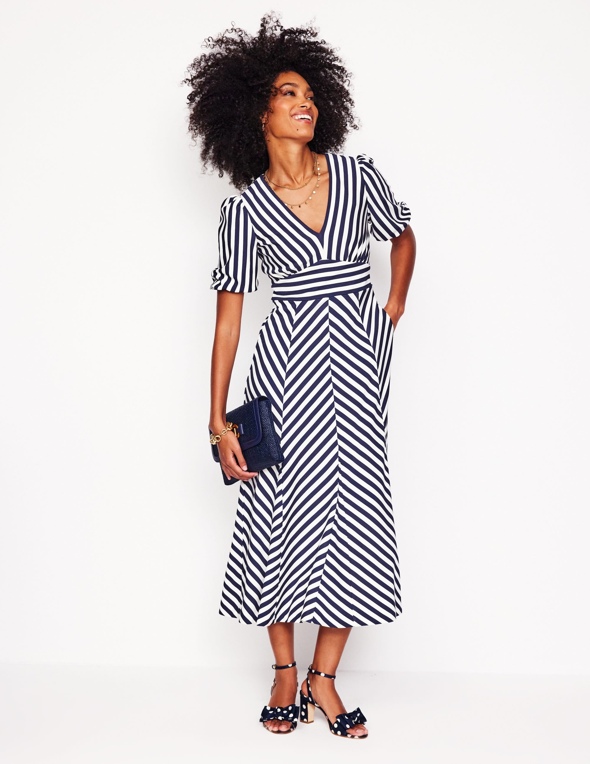A woman wearing a navy and ivory striped maxi dress with blouson sleeves, standing against a white background.