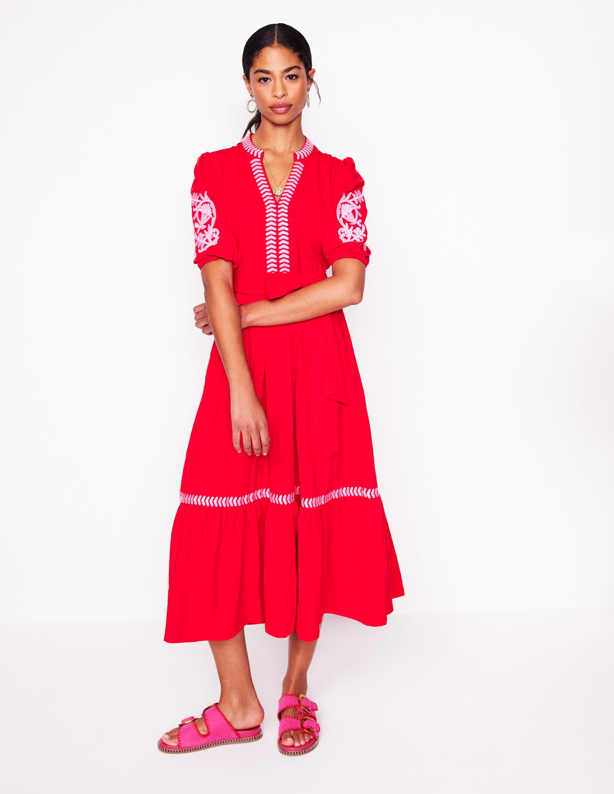 A woman wearing a red embroidered jersey dress with puff sleeves, tiered hemline, and a detachable belt.