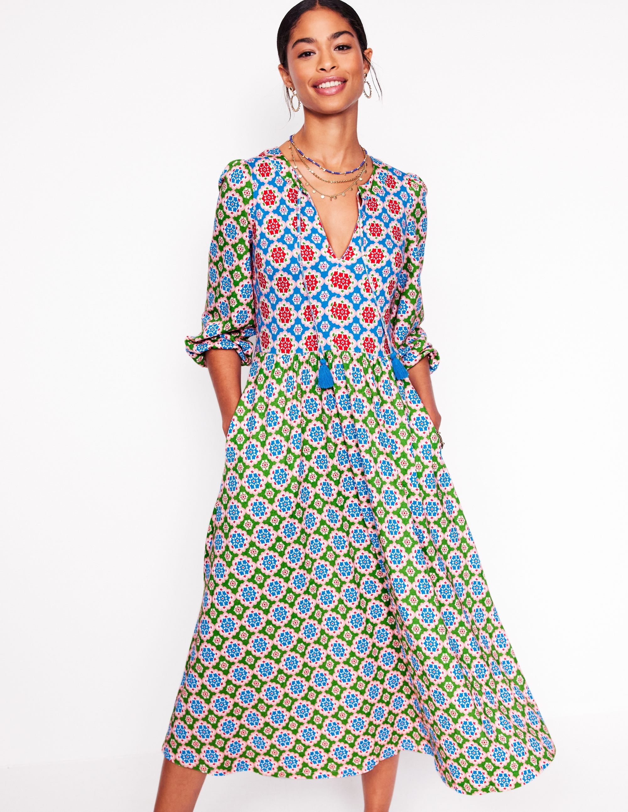 A woman wearing a multicolour floral midi dress with a notch neckline, balloon sleeves with cuffs, and tassel details.