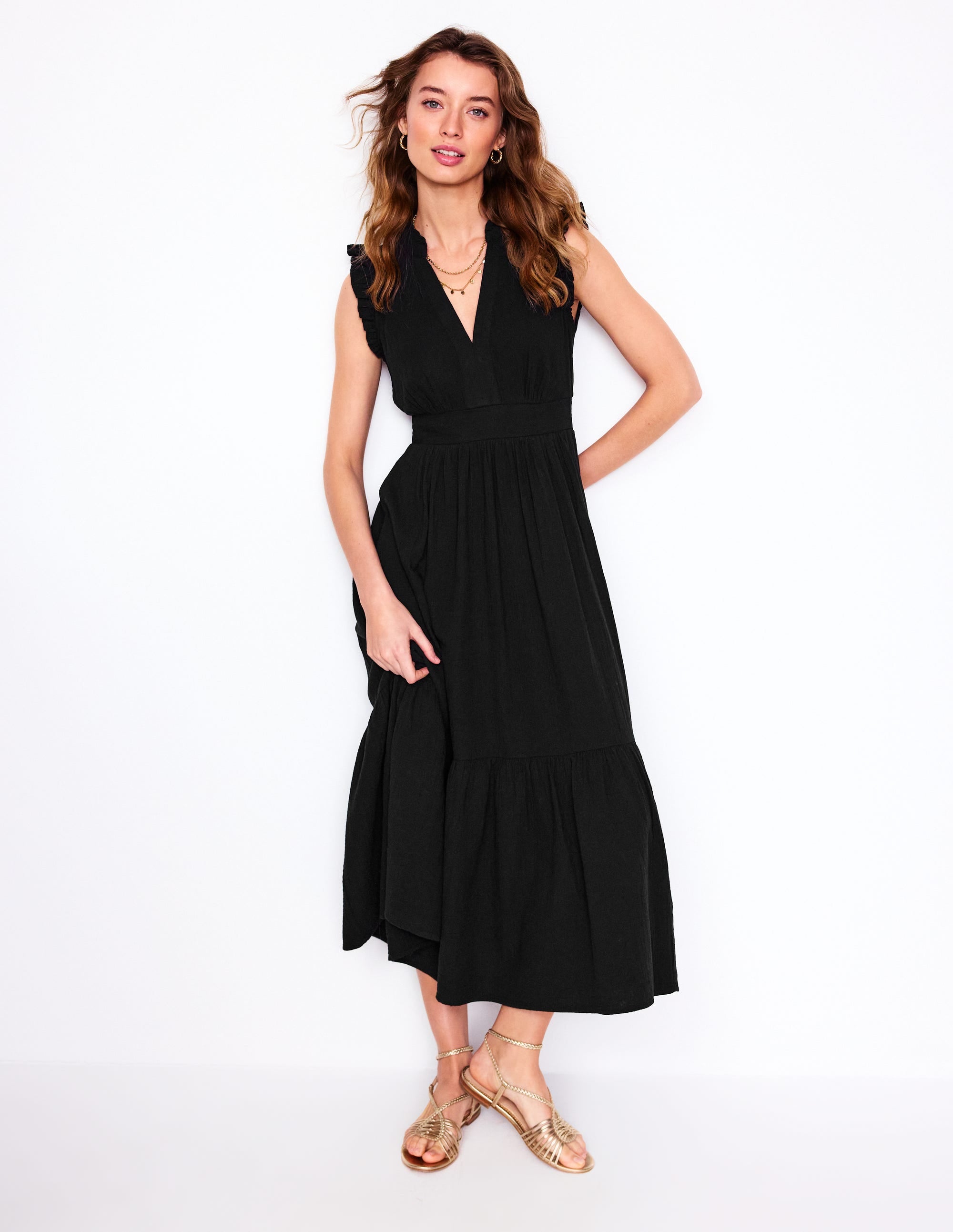A woman wearing a black midi dress with ruffled sleeves and a cinched waist, standing against a white background.