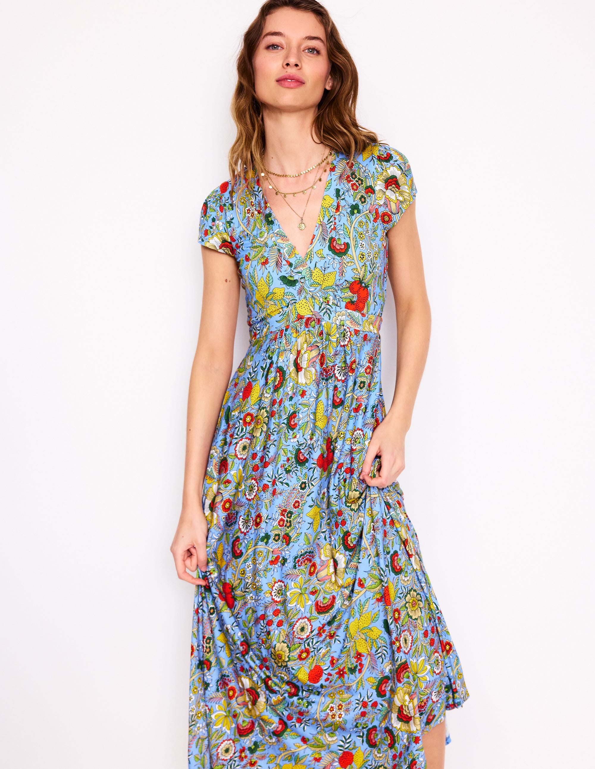 A woman wearing a multicolour floral midi dress with cap sleeves and a V-neckline, on a light blue background.