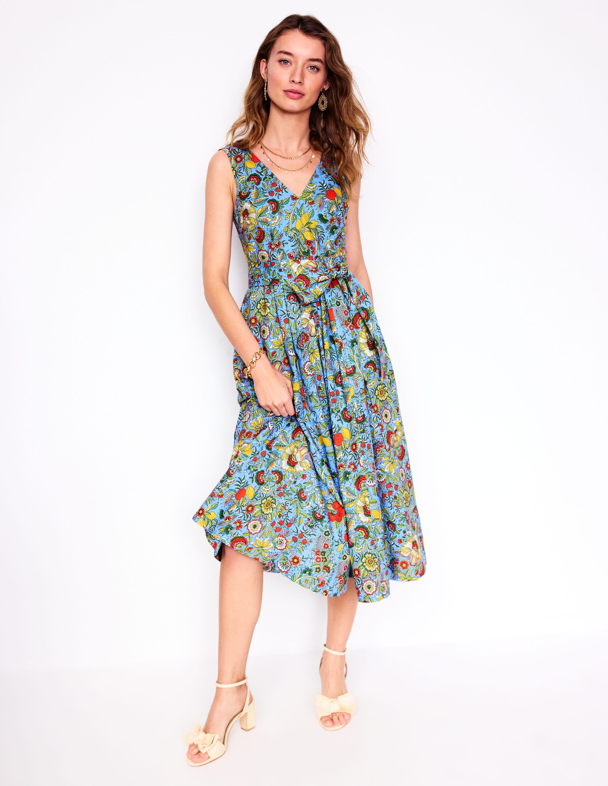 A woman wearing a multicolour floral midi dress with a V-neck, belted waist with a large bow, side pockets, and a lined bodice.