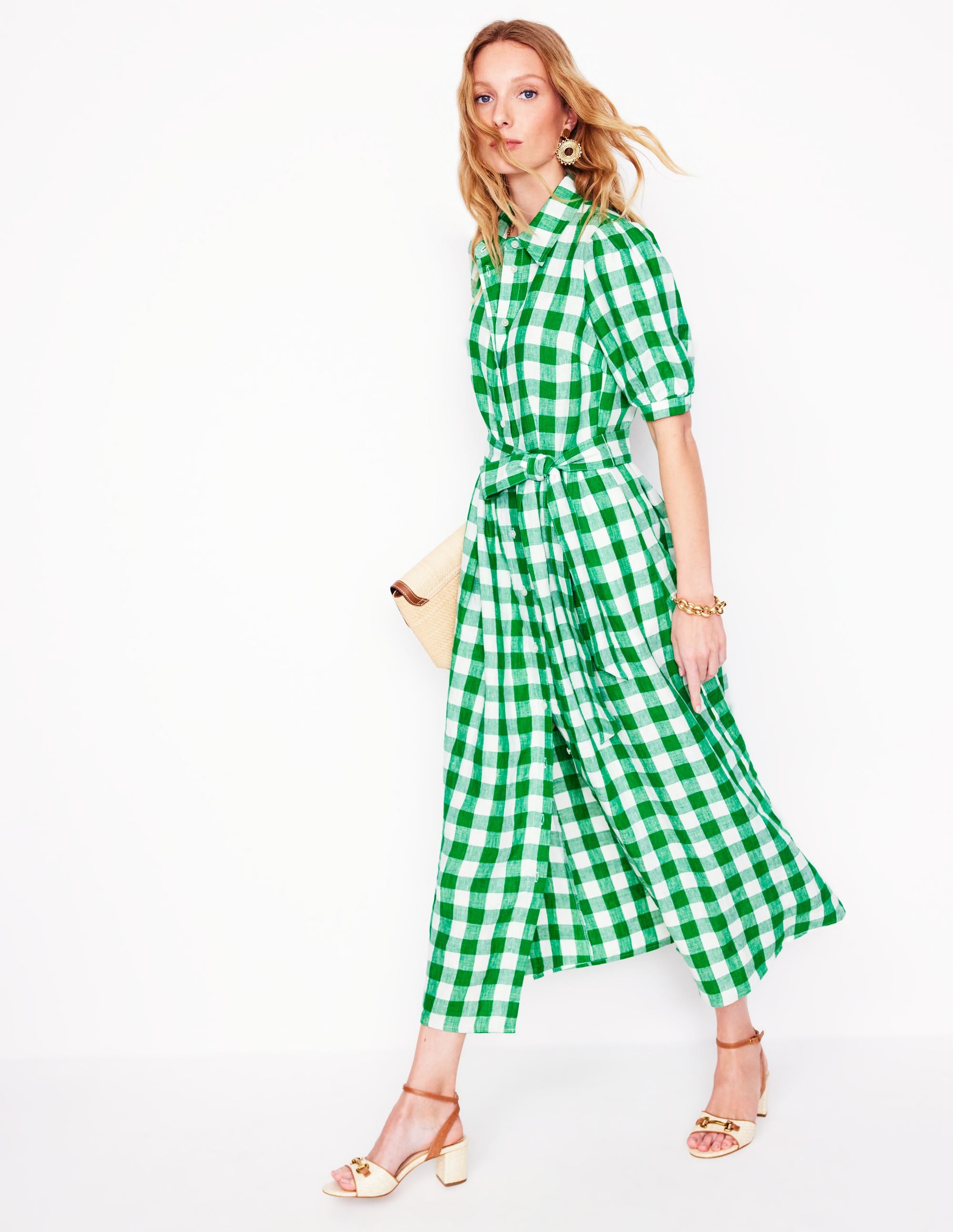 A woman wearing a green and white gingham maxi shirt dress with short puff sleeves, a waist tie, and side pockets, standing against a plain background.