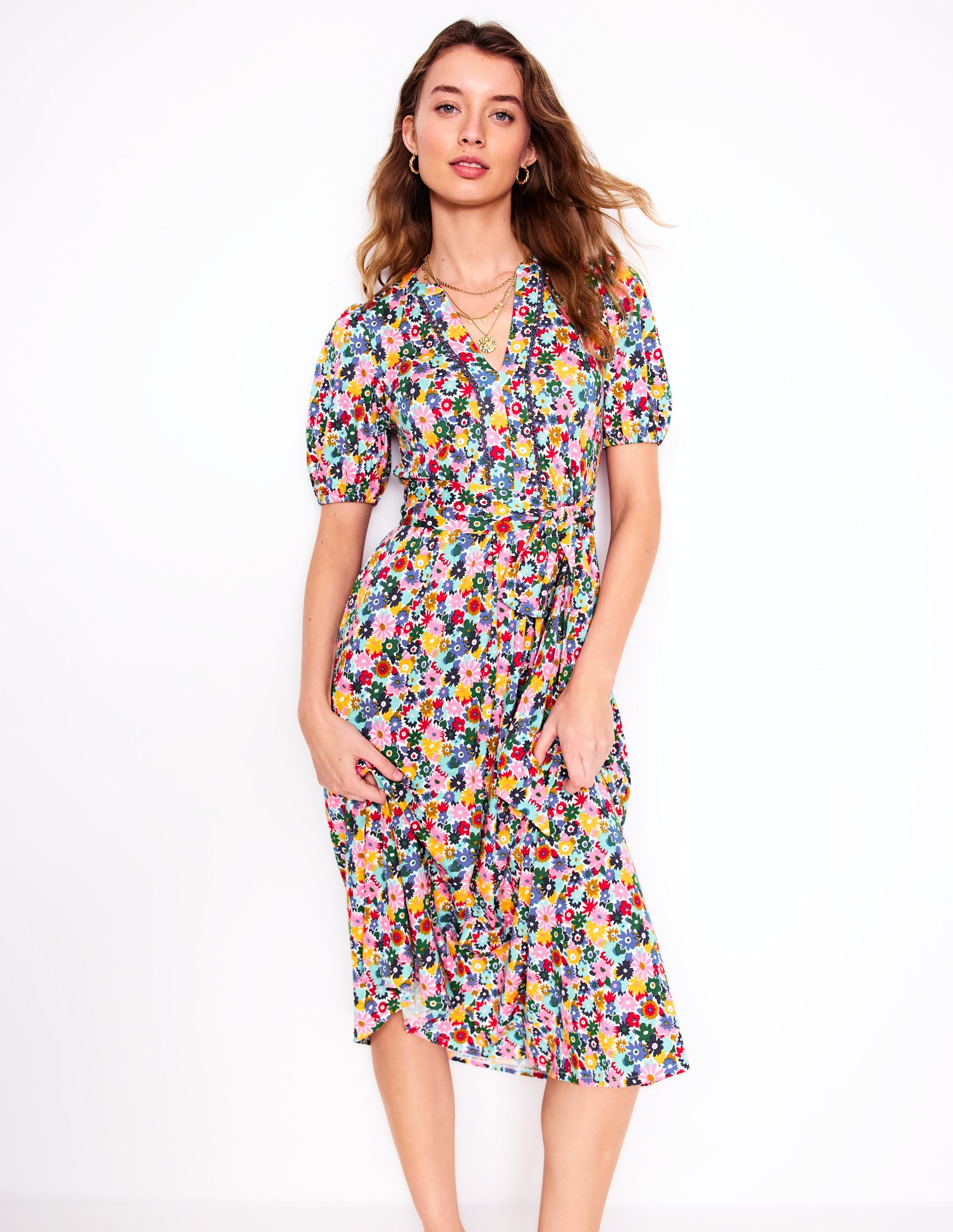 A woman wearing a multicolour floral midi dress with puff sleeves, scallop trim, and a belt, standing against a white background.