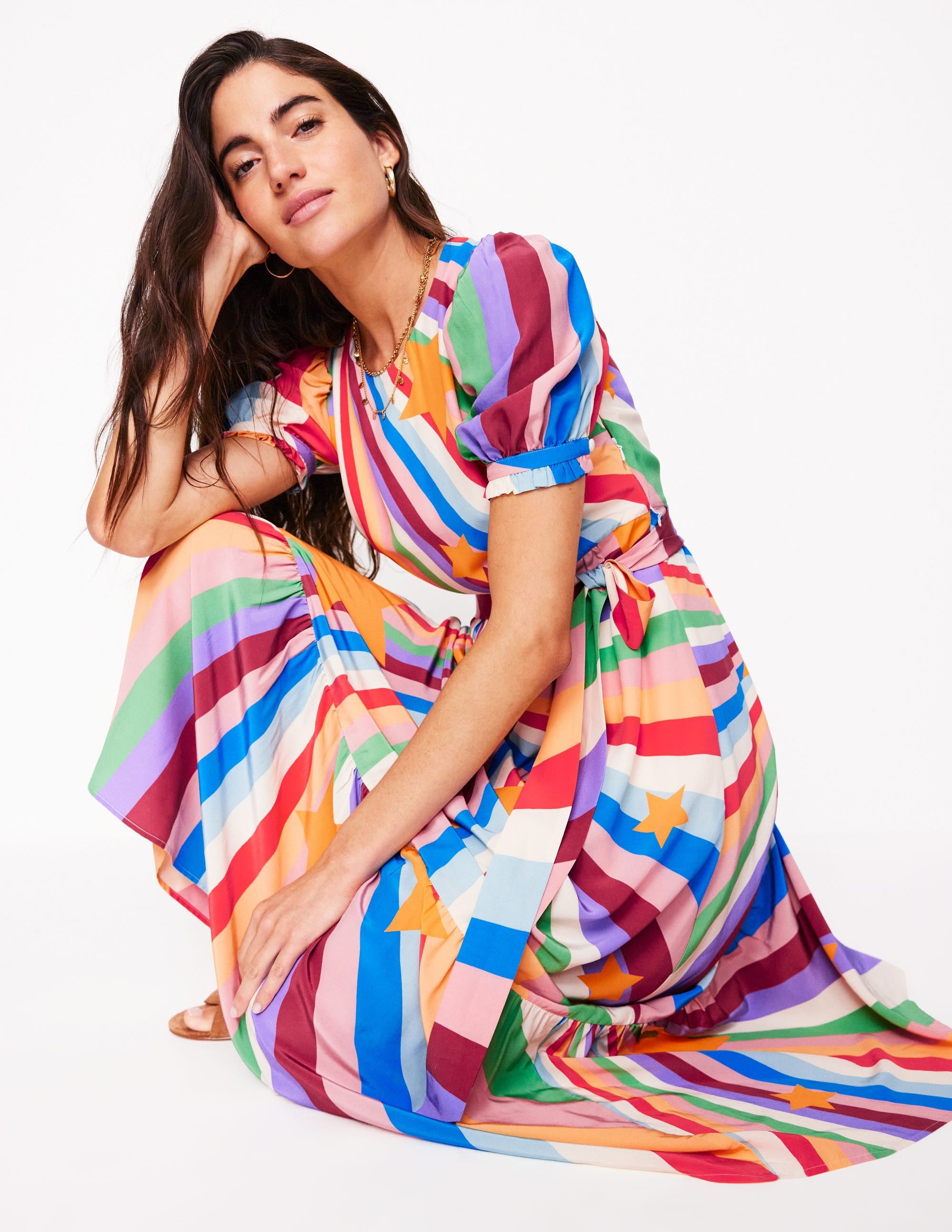 A woman wearing a multicolour, patterned maxi dress with a floaty skirt, cuffed sleeves, and a crew neck, standing against a white background.