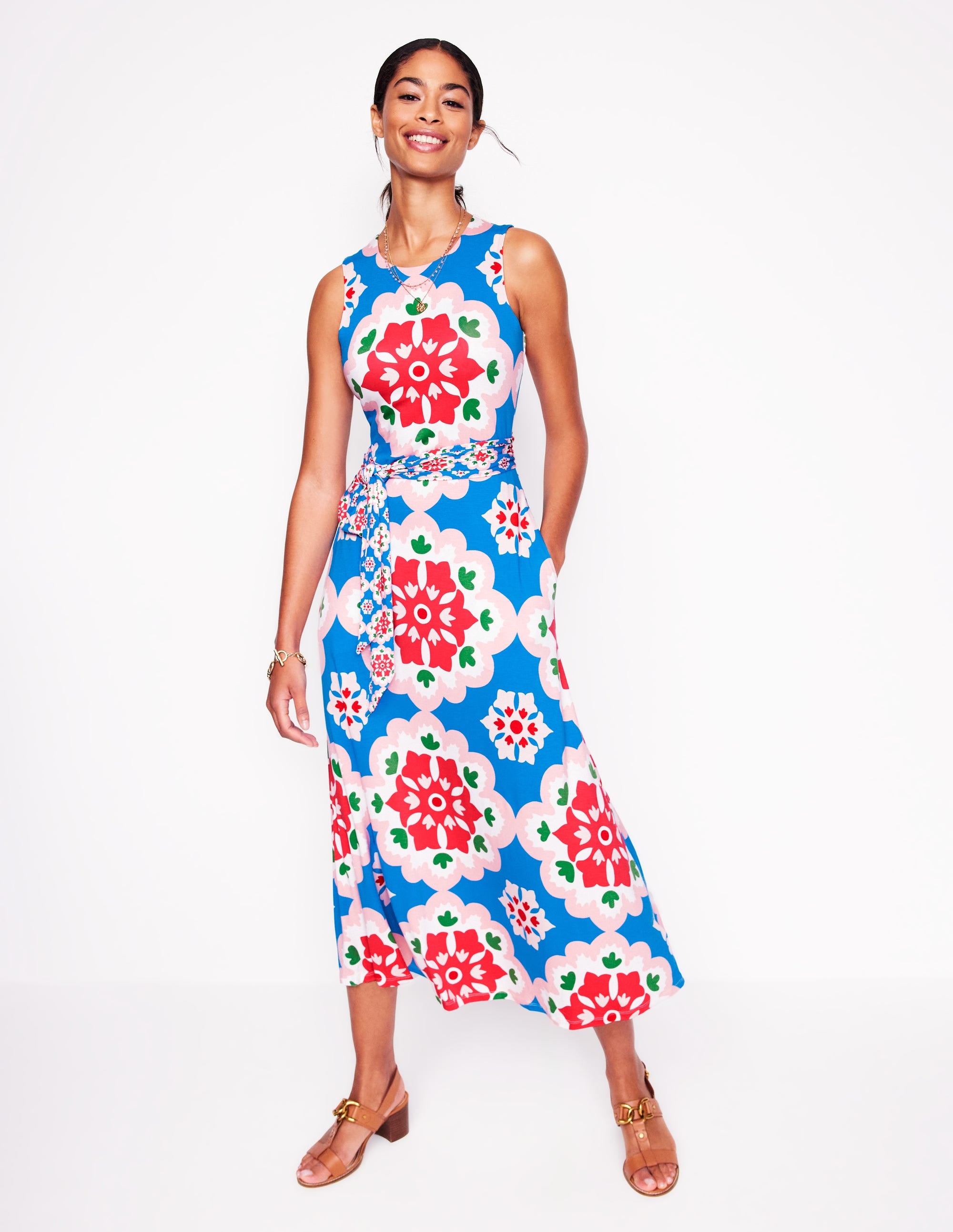 A woman wearing a sleeveless, floral patterned maxi dress with a tie waist, lined bodice, and side pockets.