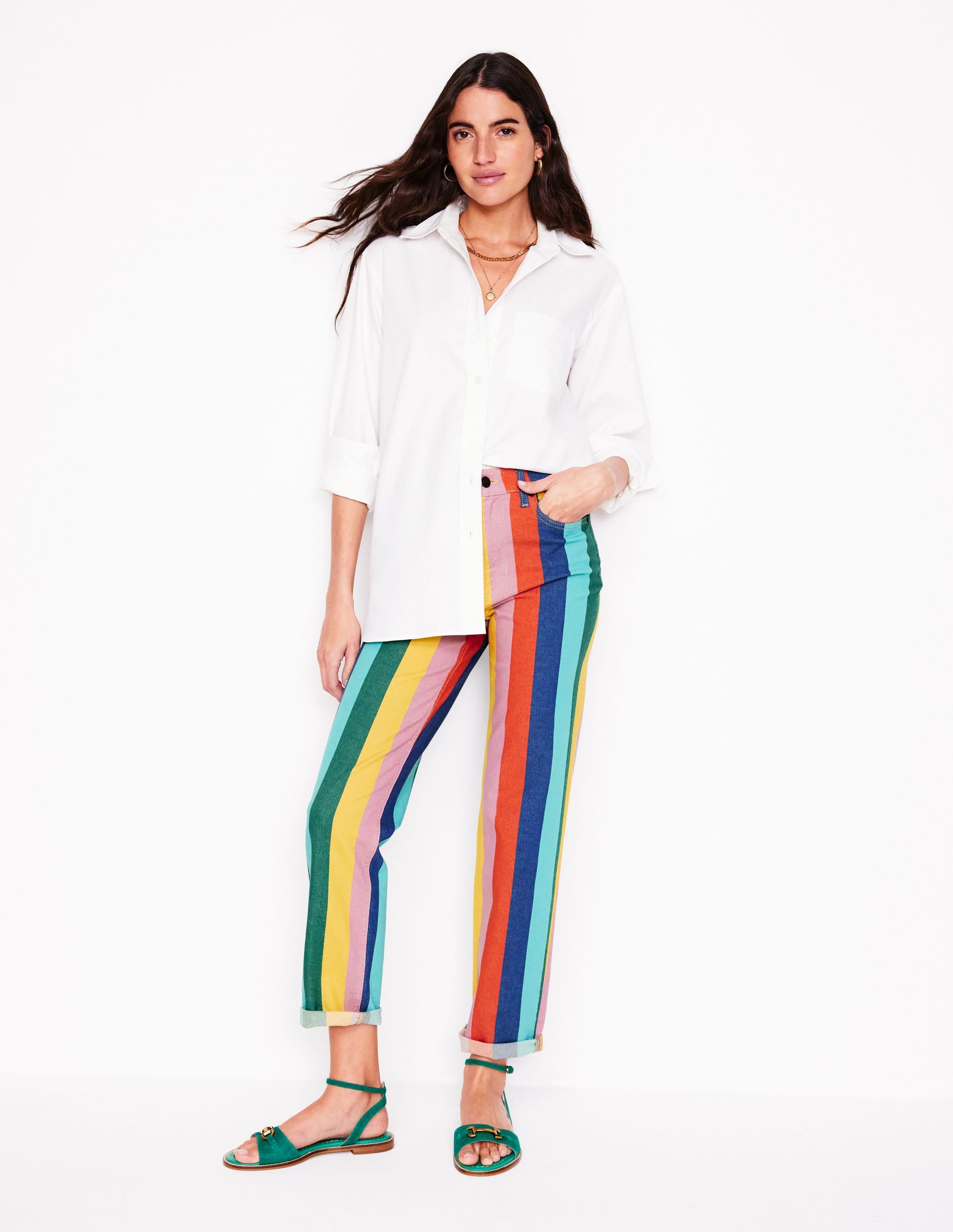 A woman wearing high-rise, multi-colored striped jeans with a white shirt and green sandals.