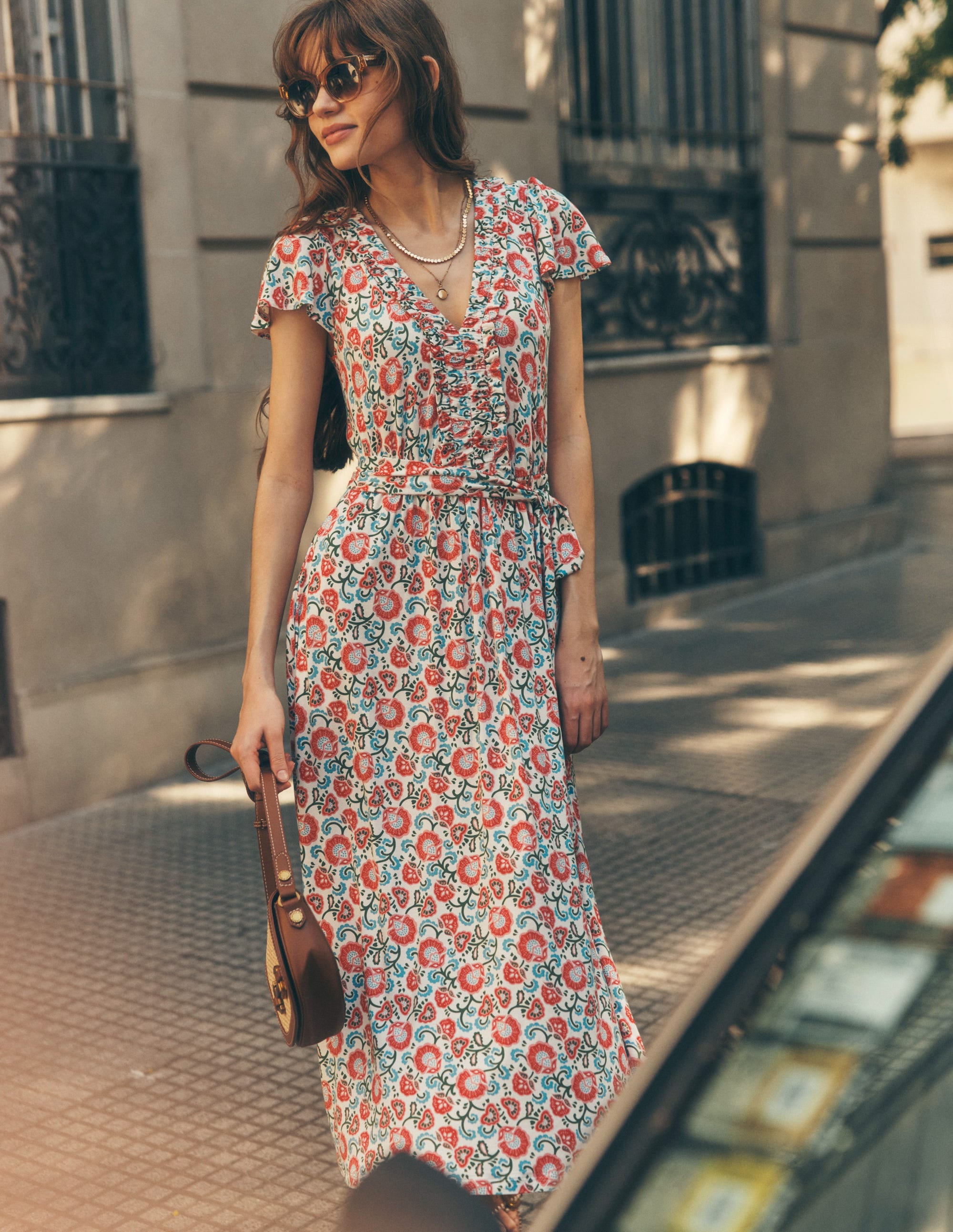 A woman wearing an ivory floral midi dress with short ruffled sleeves, a fitted bodice, and a flowy skirt, standing outdoors.