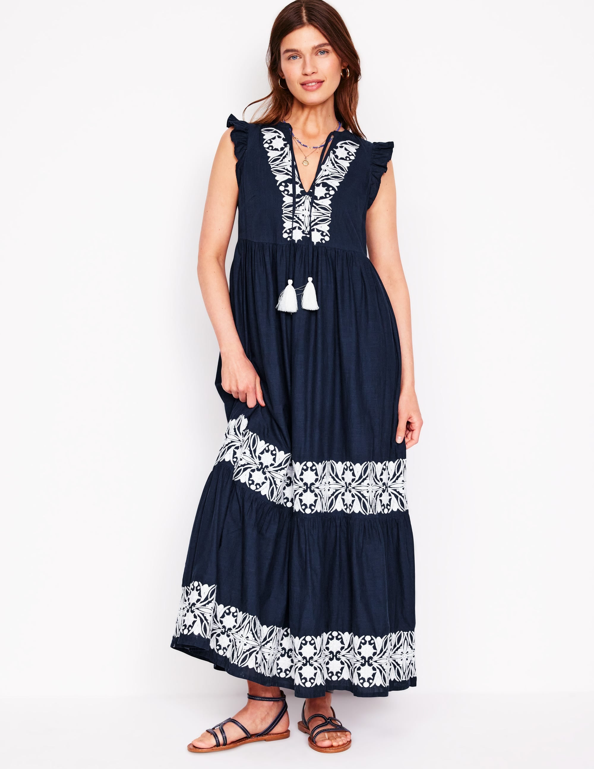 A woman wearing a navy tiered dress with white embroidery, ruffled shoulder details, and tassels at the neckline.