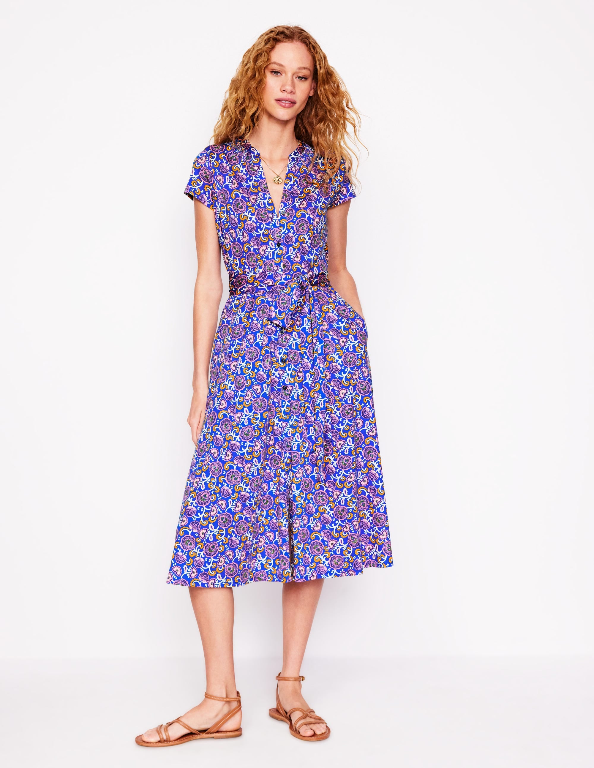 A woman wearing a blue jersey shirt dress with a garden vine pattern, short sleeves, and a smocked neckline, standing against a white background.