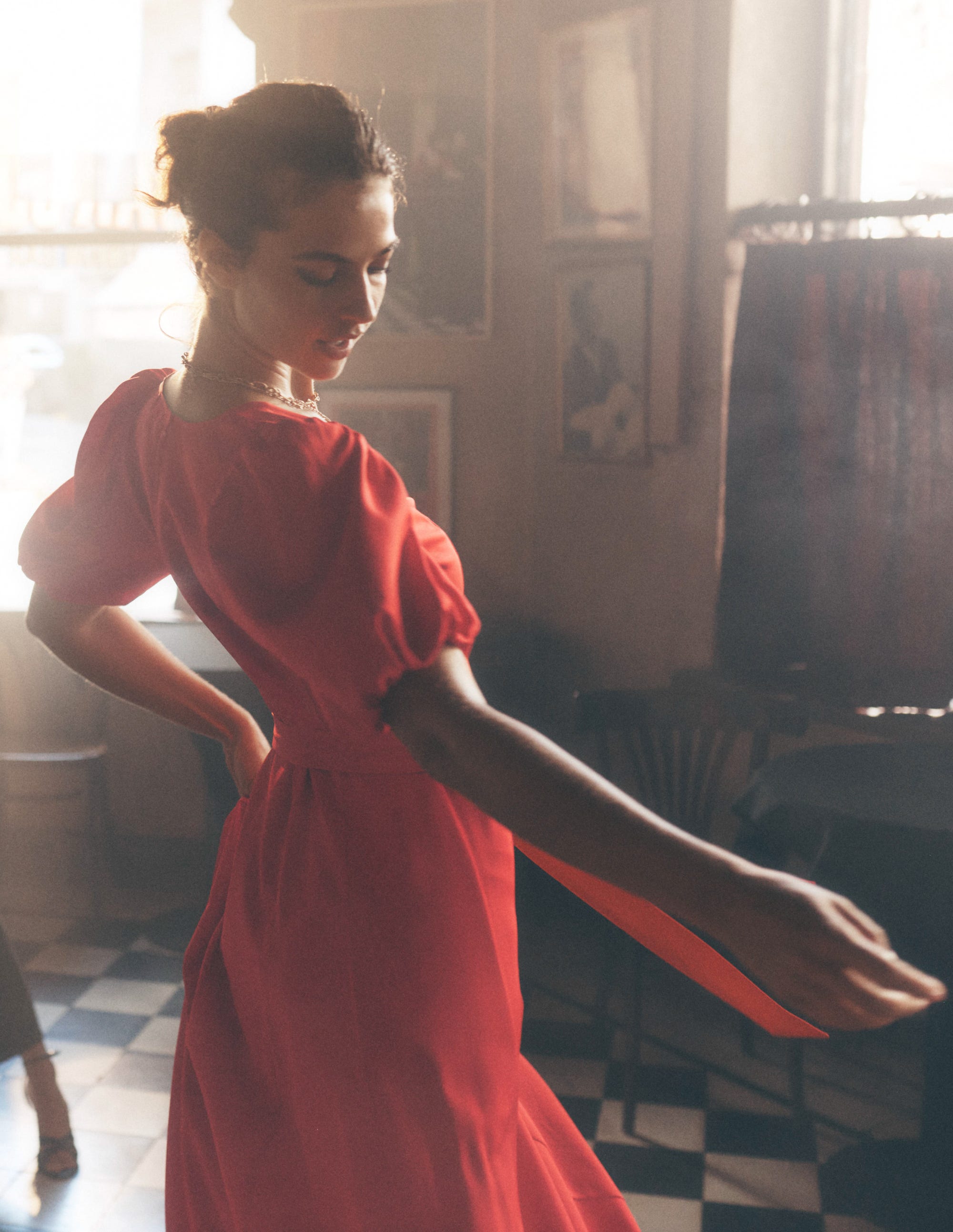 A woman wearing a red midi dress with puff sleeves, standing indoors with a vintage decor background.