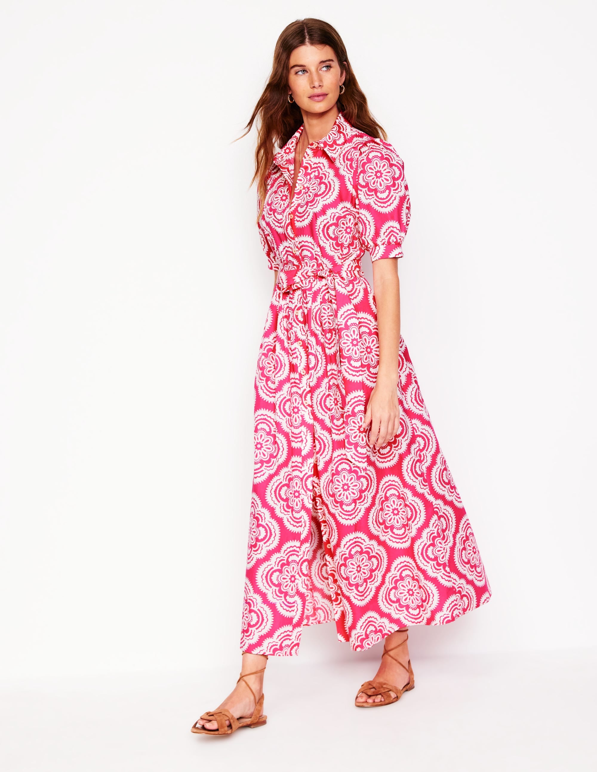 A woman wearing a pink floral maxi shirt dress with puff sleeves, a belted waist, and side pockets.