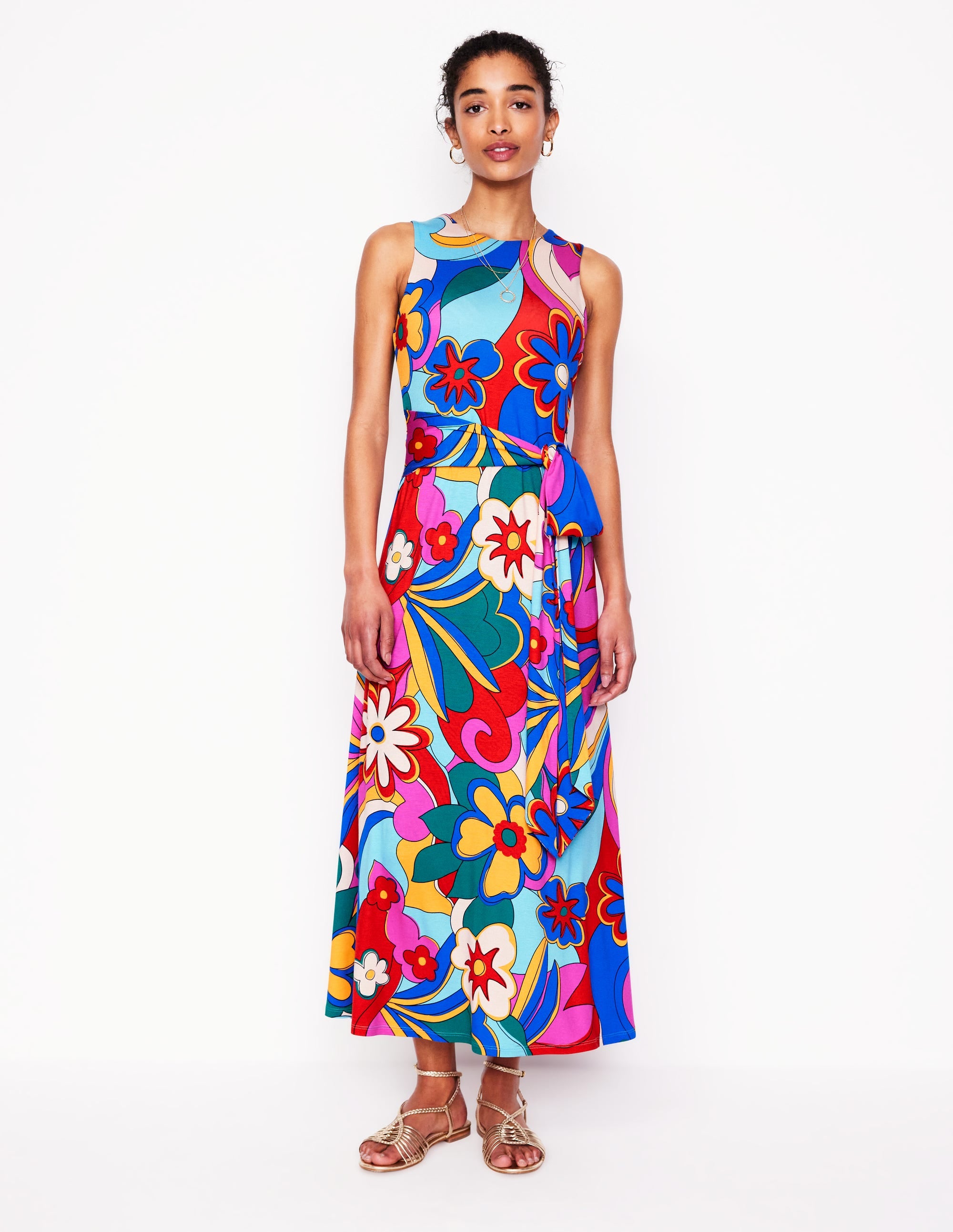 A woman wearing a sleeveless, multicolour floral maxi dress with a self-fabric belt, side pockets, and a lined bodice.