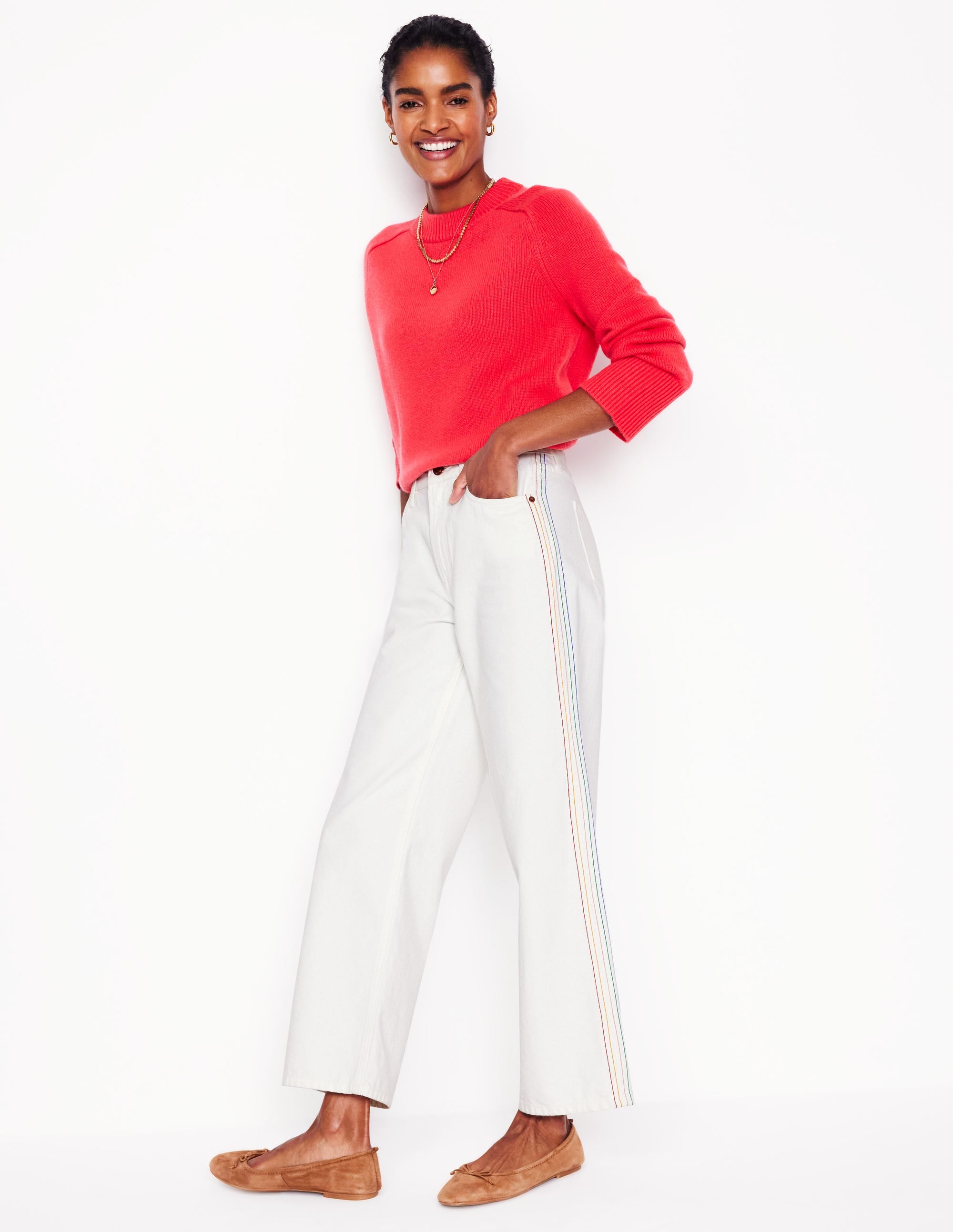 A pair of high-rise, off-white, straight crop jeans with embroidery details on the side seams, worn by a woman with her hand in her pocket.
