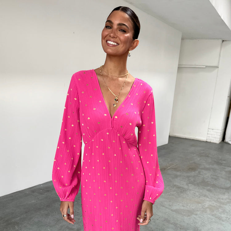 A woman wearing a bright pink dress with gold flecks, long sleeves, and a V-neckline with a hook and eye fastening.