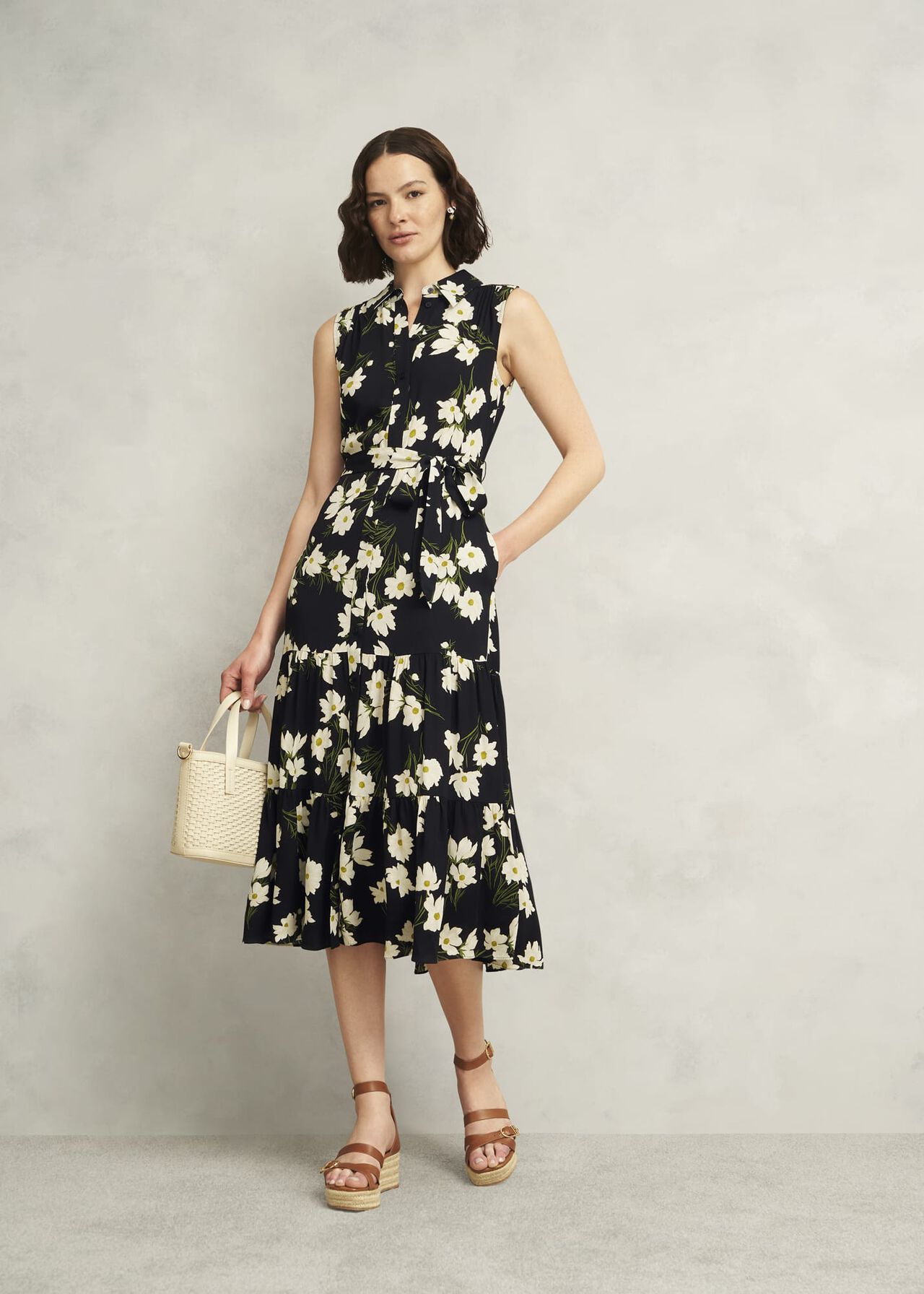 A woman wearing a navy floral midi dress with a collar, sleeveless design, and a tie waist, standing against a plain background.