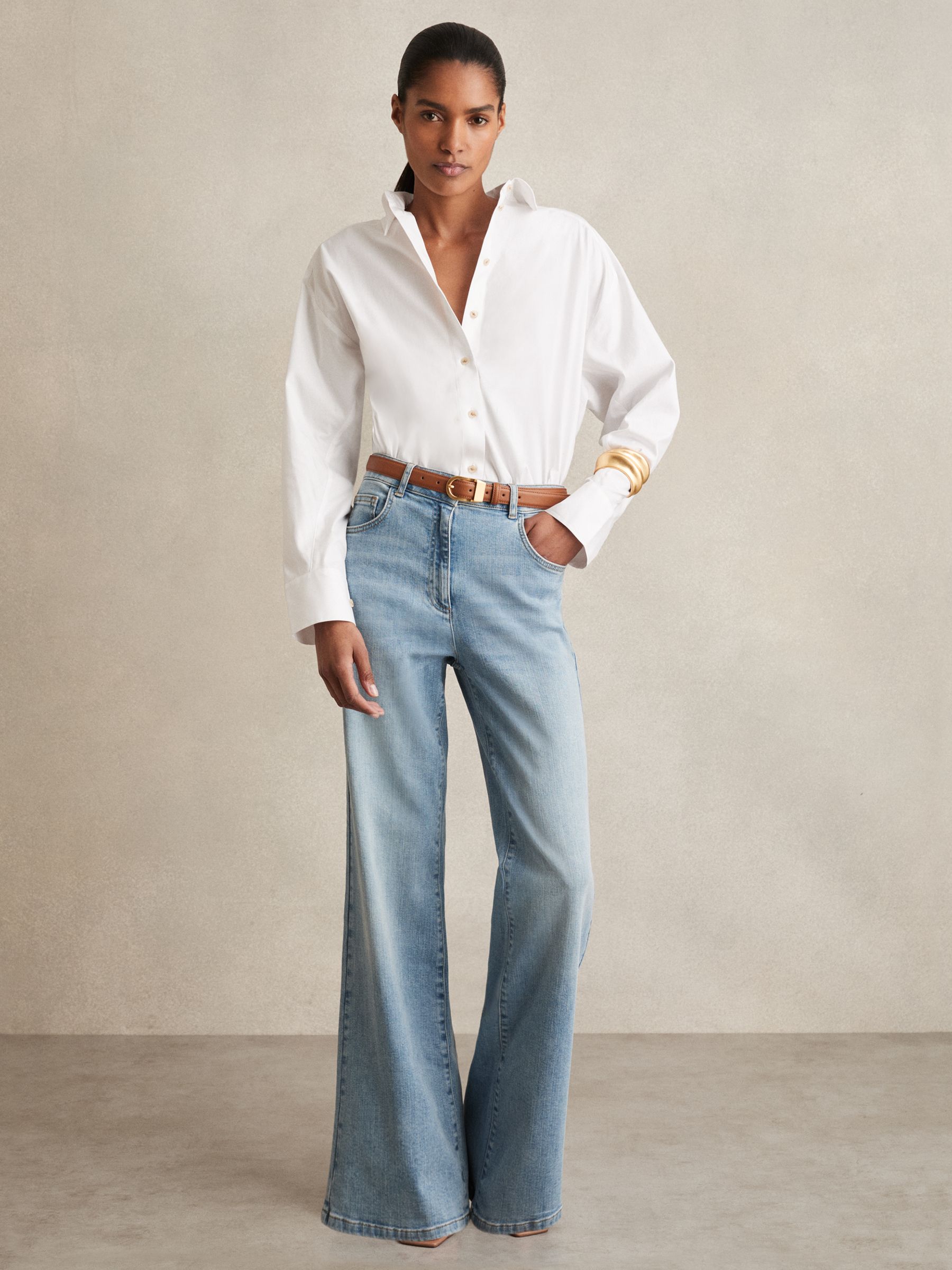 A woman wearing light blue mid-rise flared jeans with five pockets, a front button, and a zip closure, paired with a white shirt.