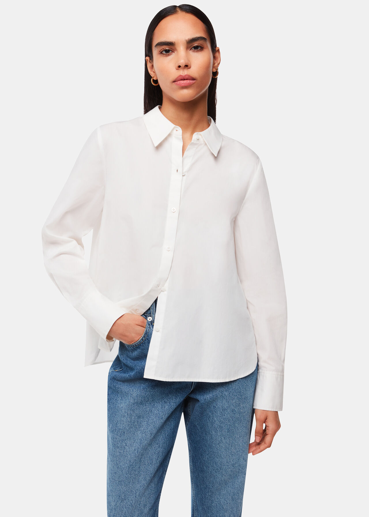 A woman wearing a white boxy cotton shirt with a collar and button closure, paired with blue jeans.