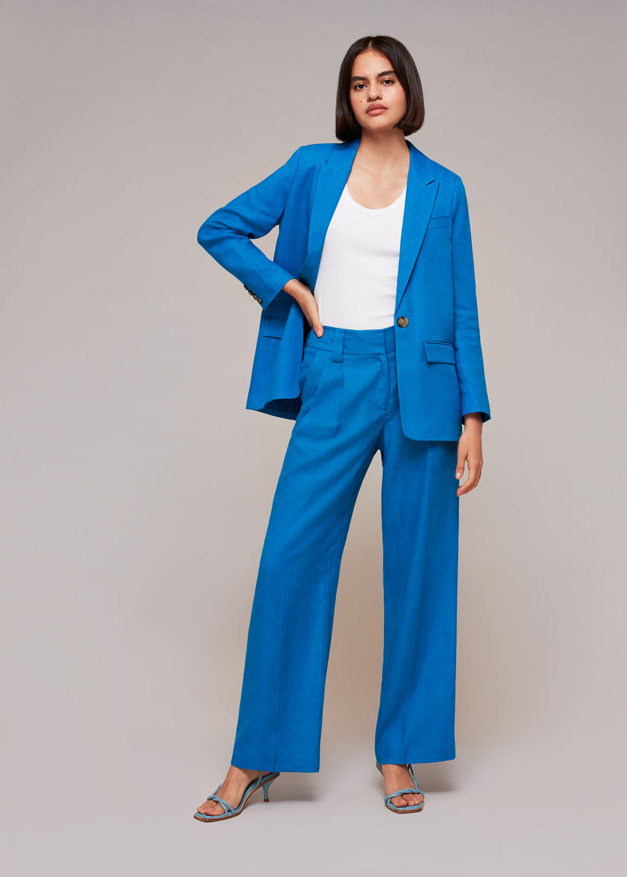 A woman wearing a bright blue linen blazer with a relaxed fit, button closure, and side pockets, paired with matching blue linen trousers and a white top.