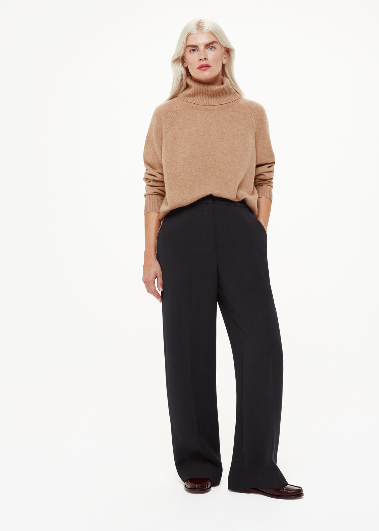 A woman wearing black full-length trousers with a high waist and straight leg, paired with a beige turtleneck sweater.