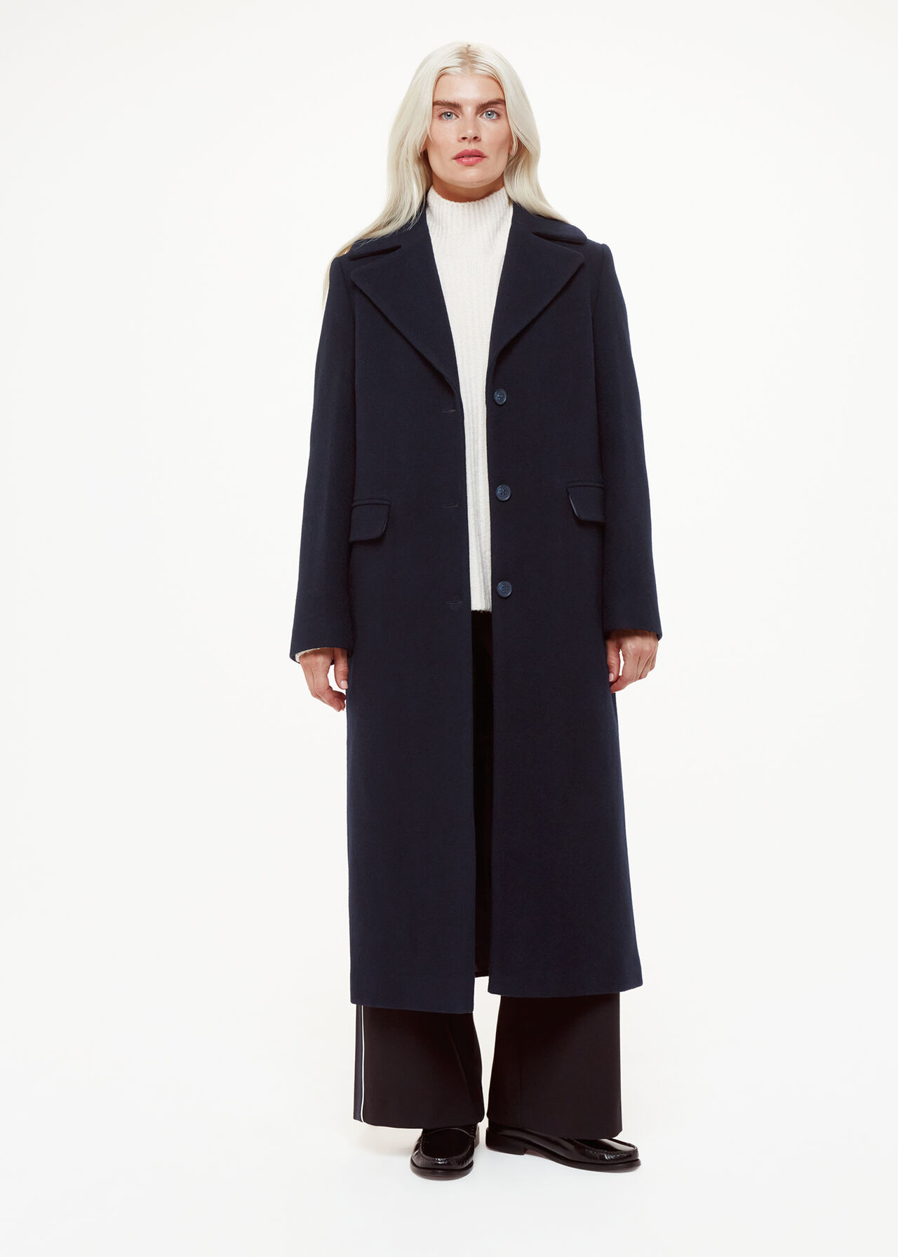 A woman wearing a navy blue longline coat with a button front, flap pockets, and a classic design.