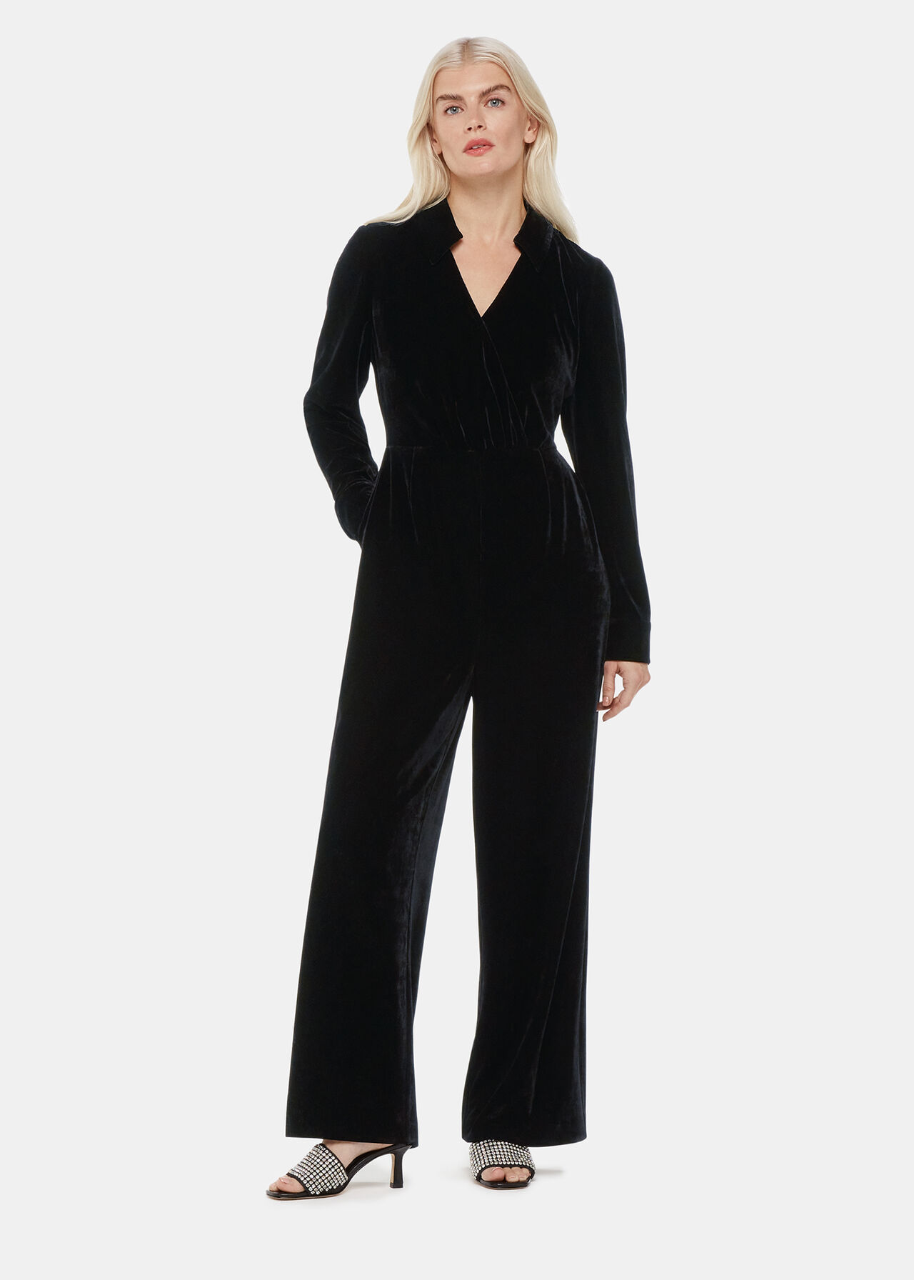 A woman wearing a black velvet wrap jumpsuit with a collared neckline and long sleeves, standing against a plain background.