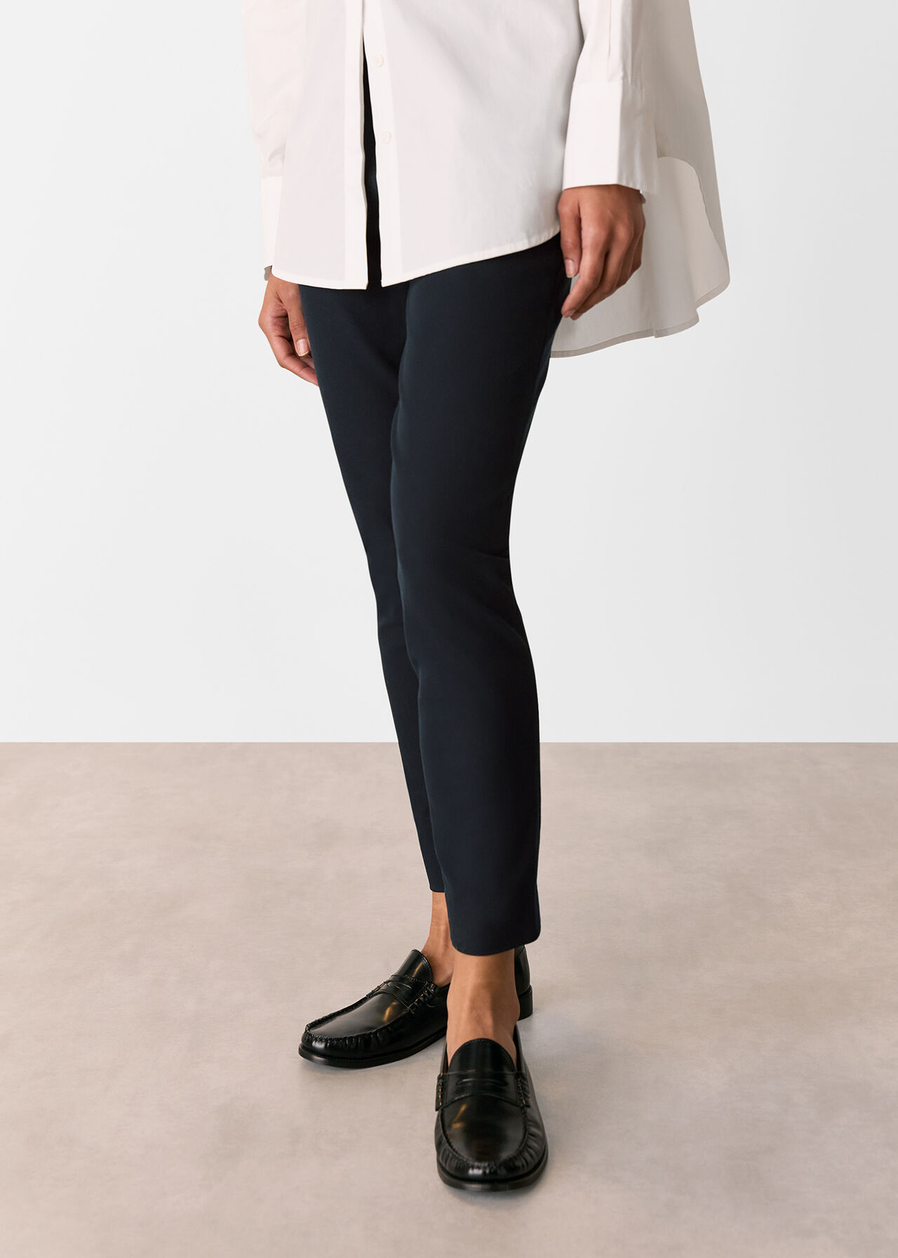 A person wearing navy tailored trousers with a hidden waistband and side zip, paired with black loafers and a white shirt.