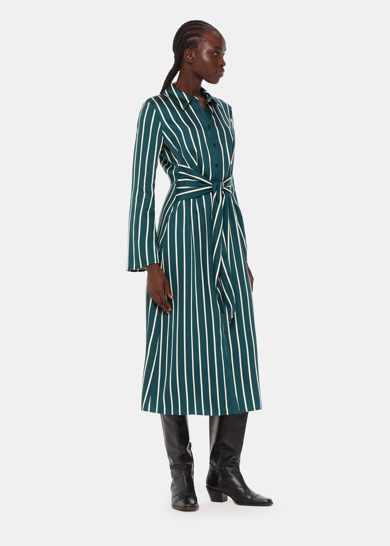 A woman wearing a green and white striped shirt dress with a collar, buttons down the front, and a waist tie, paired with black knee-high boots.
