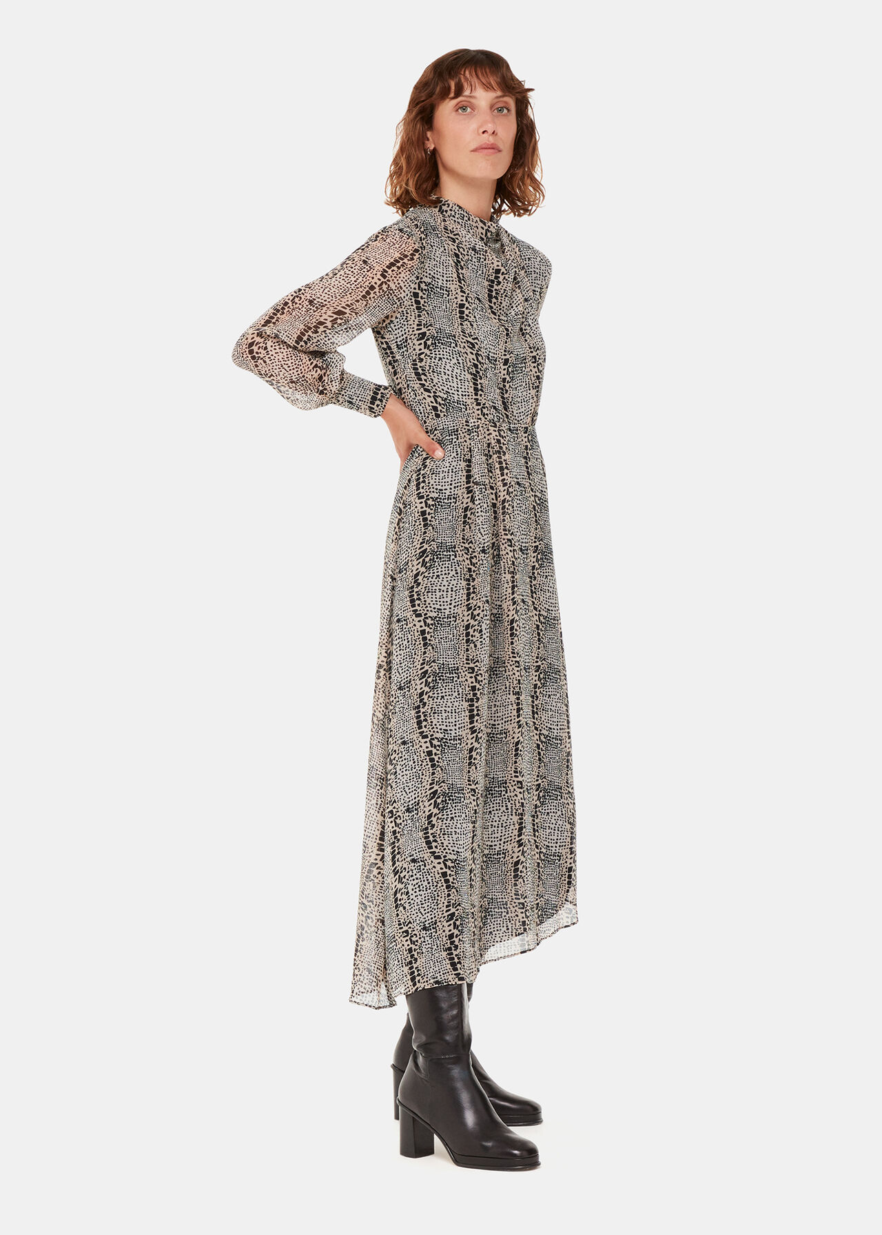 A woman wearing a multicolour optical snake print dress with long sleeves, a high neckline, and a fitted waist, paired with black knee-high boots.