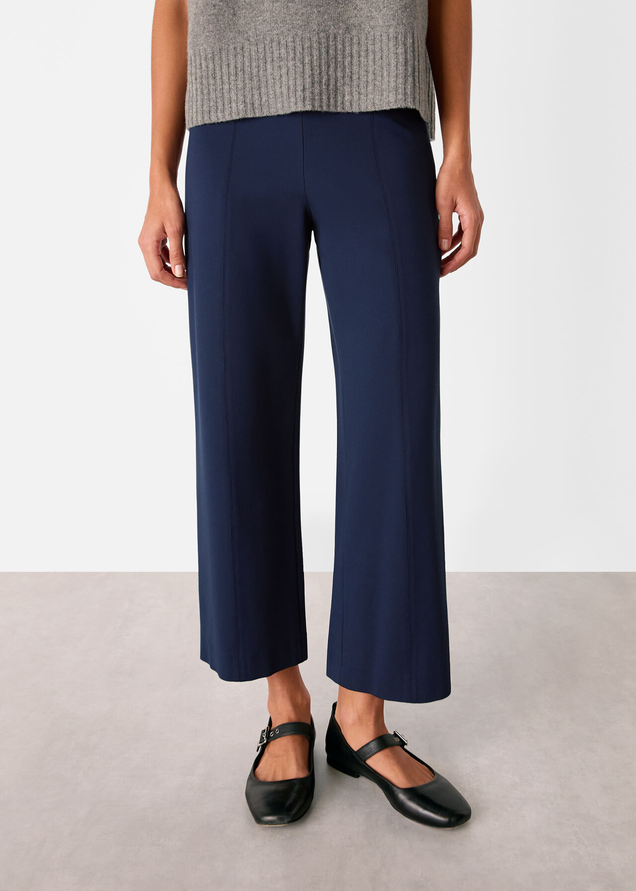 A pair of navy wide-leg trousers with a cropped length and fitted waist, styled with black shoes and a grey top.