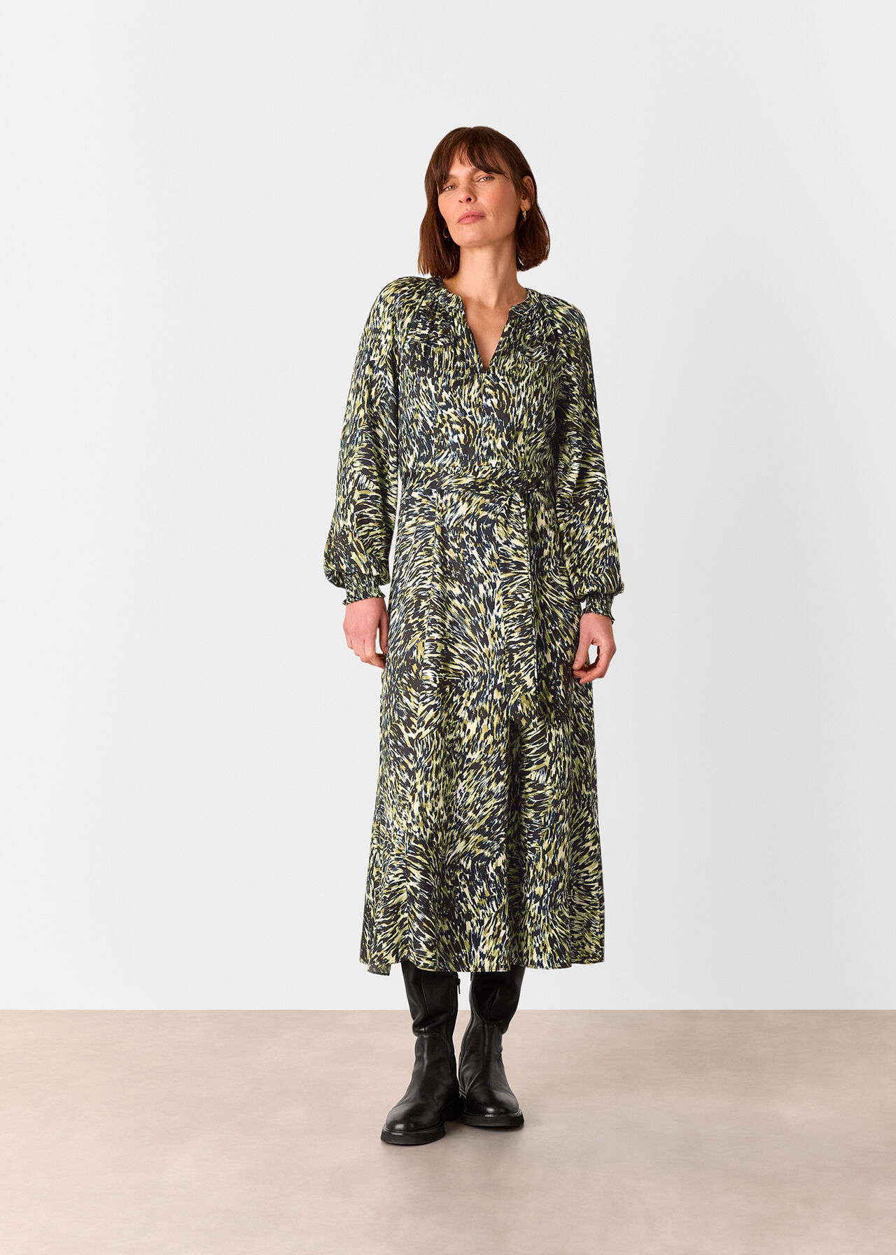 A woman wearing a midi dress with a leopard swirl print in shades of blue, khaki, and yellow, featuring a V-neckline, long cuffed sleeves, and a waist belt.